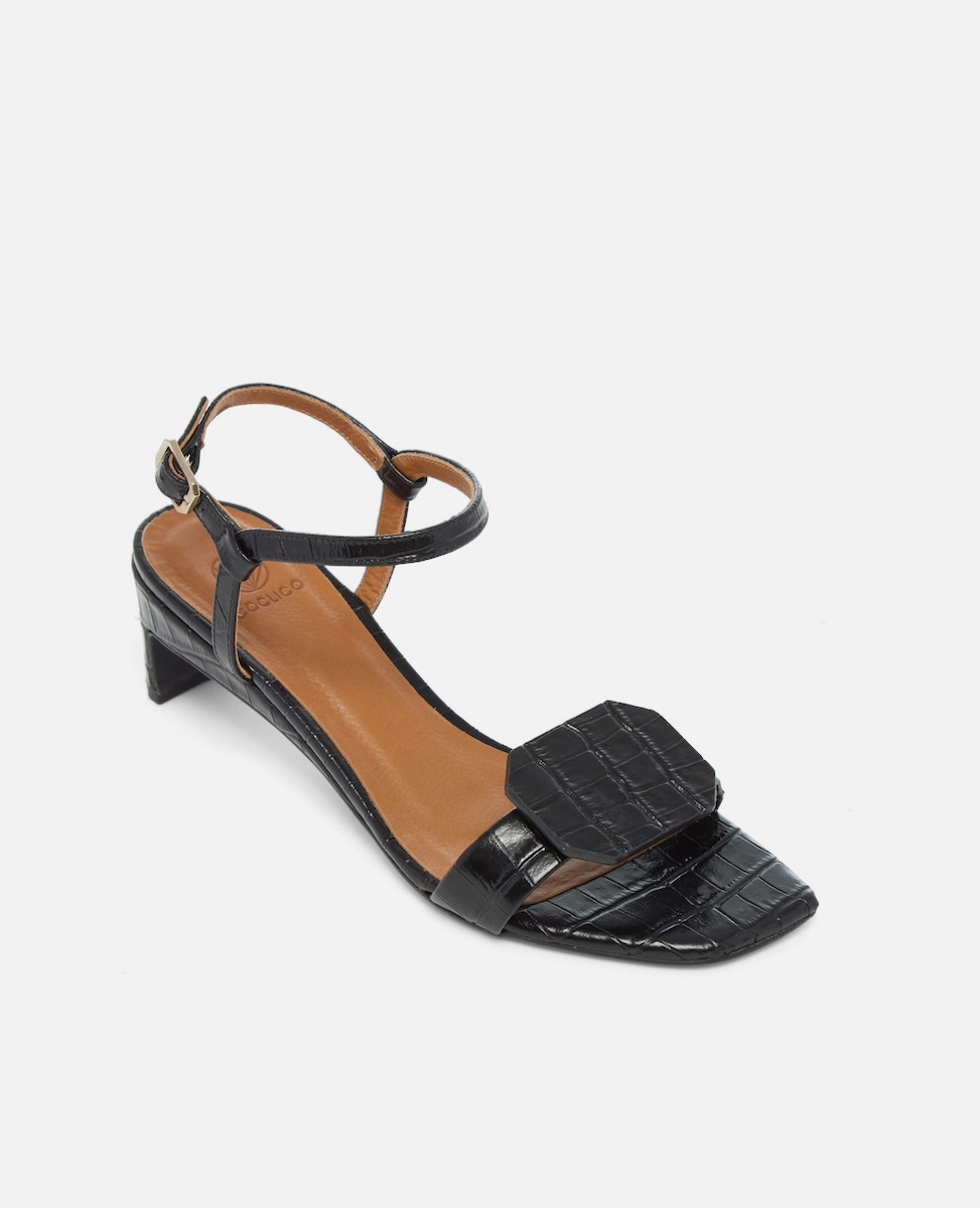 Angled view of a black croc-embossed leather sandal with a slim ankle strap, octagonal toe detail, and a low wrapped demi heel on a white background