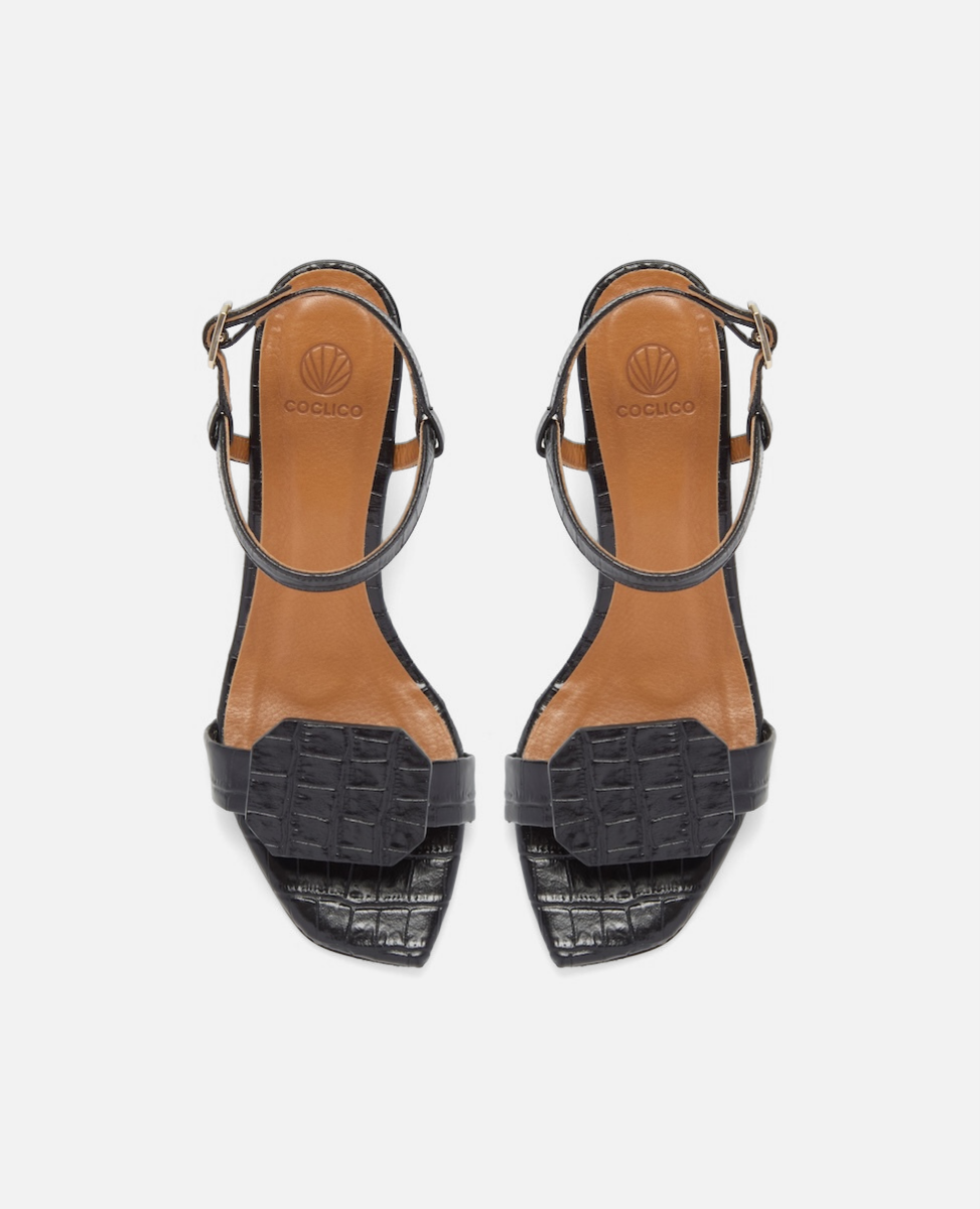 Top view of a black croc-embossed leather sandal with a slim ankle strap, octagonal toe detail, and a low wrapped demi heel on a white background