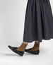 Shiny black leather loafers with a sleek, low-profile design, paired with ribbed brown socks and a long, dark gray skirt. 2