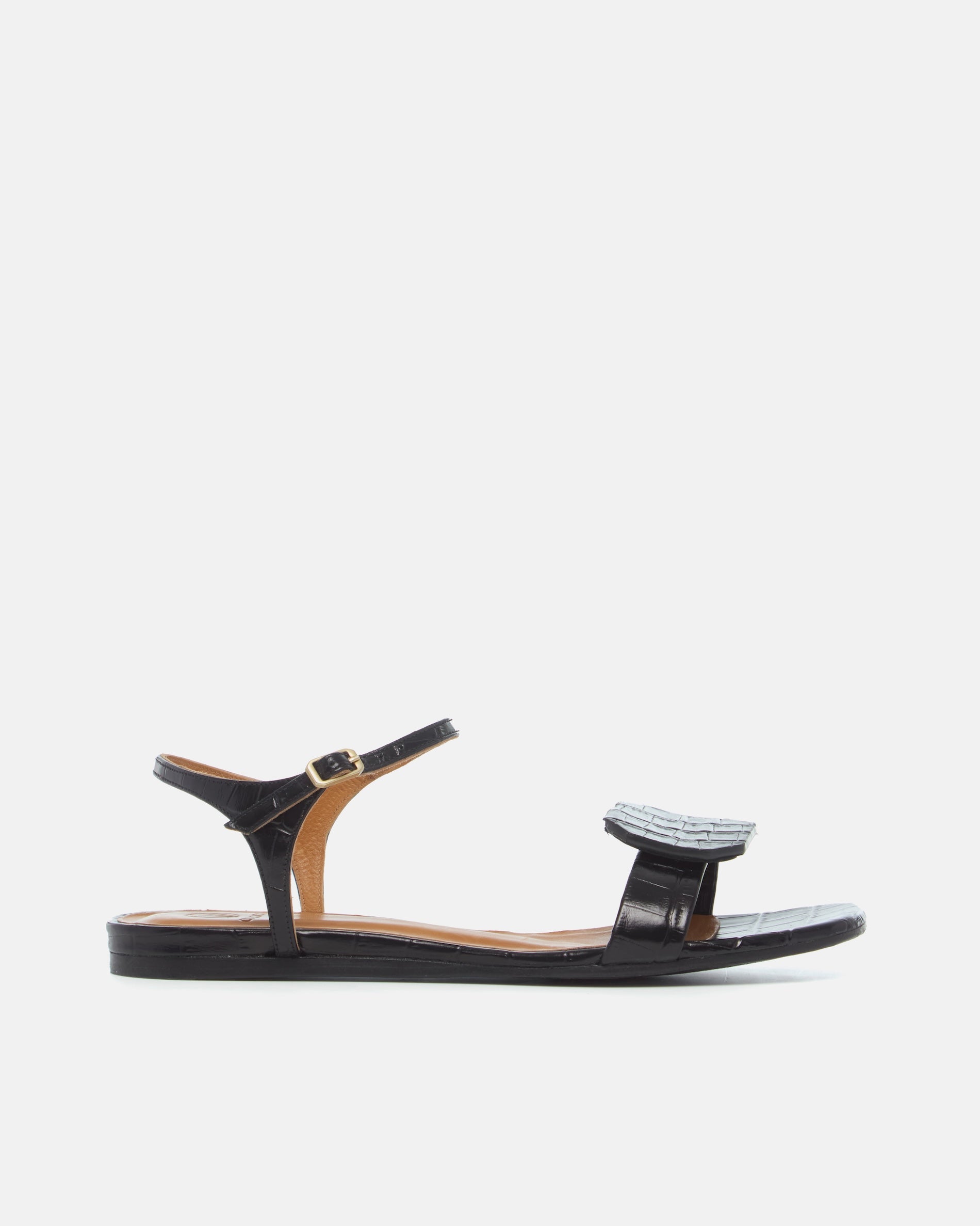 Side view of a black croc-embossed leather flat sandal with a slim ankle strap and a octagonal accent on the front strap, square toe, on a white background.