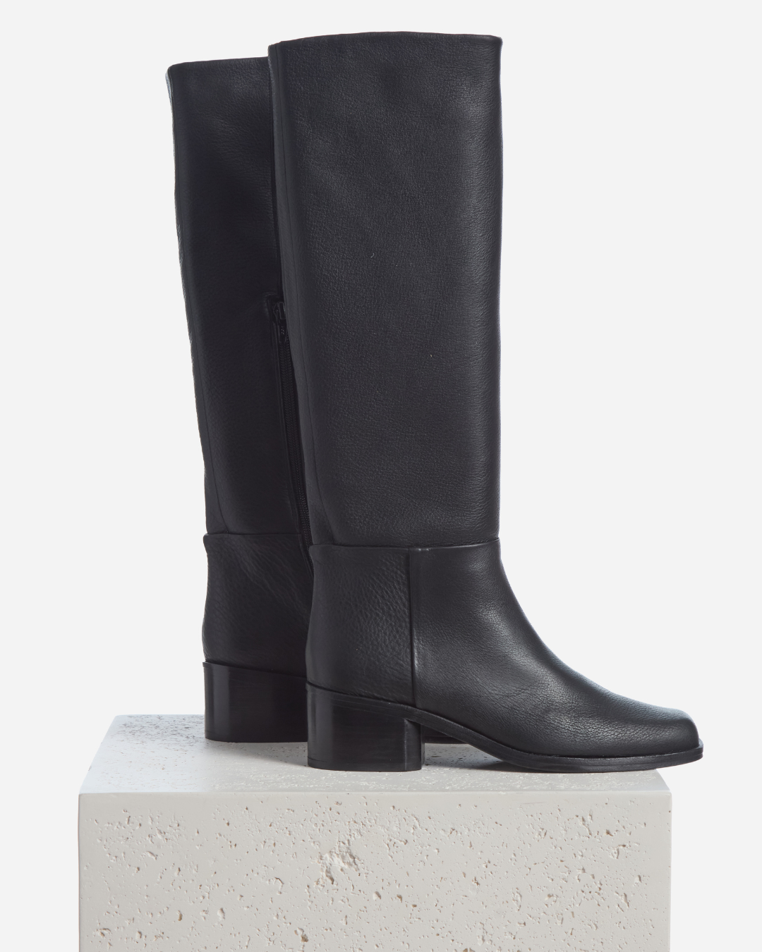 Coclico Alto Boot in black leather, knee high boots with low block heels styled on a stone plinth