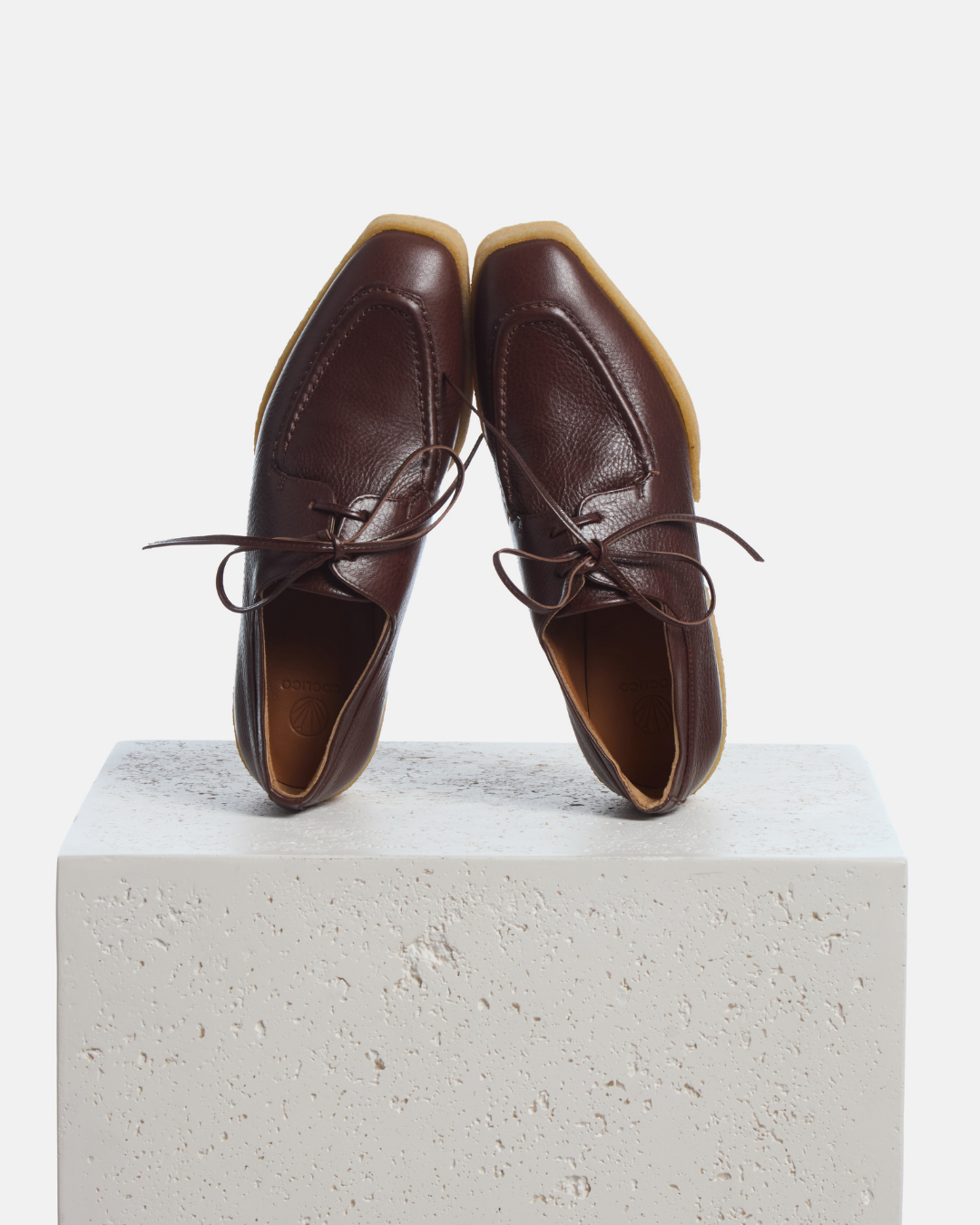 Coclico Butler Oxford in Castagno leather, brown lace up oxfords with natural crepe soles styled on a stone plinth