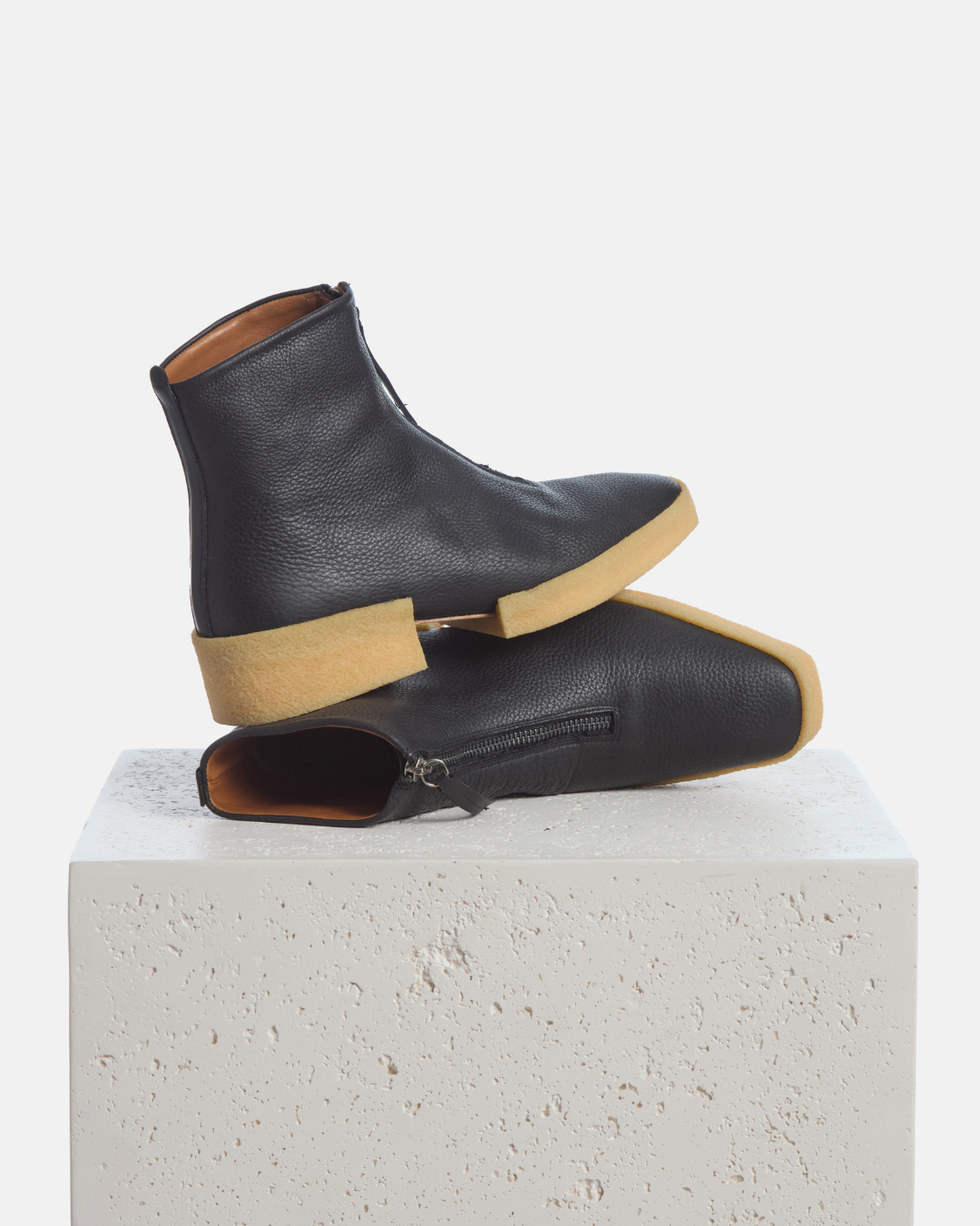 Coclico Buzz Boot in black leather, front zip ankle boots with natural crepe soles styled on a stone plinth