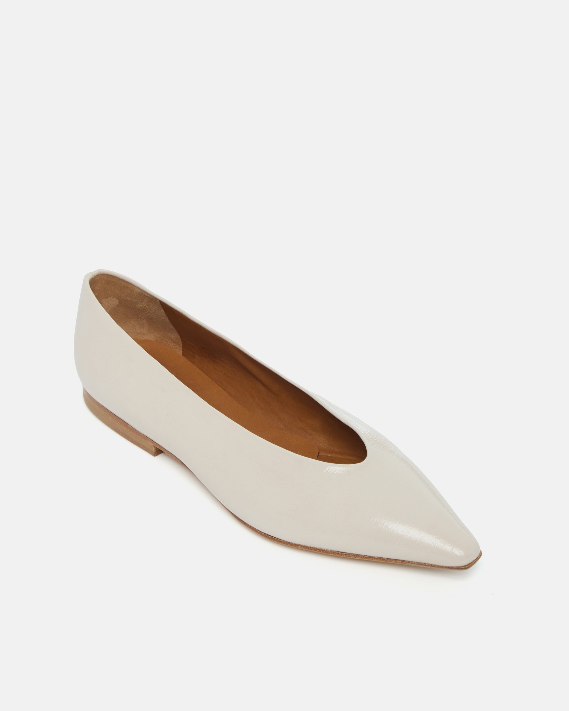 Angled view of a off-white patent leather pointed-toe flat with clean lines and a flexible leather sole, on a white background.