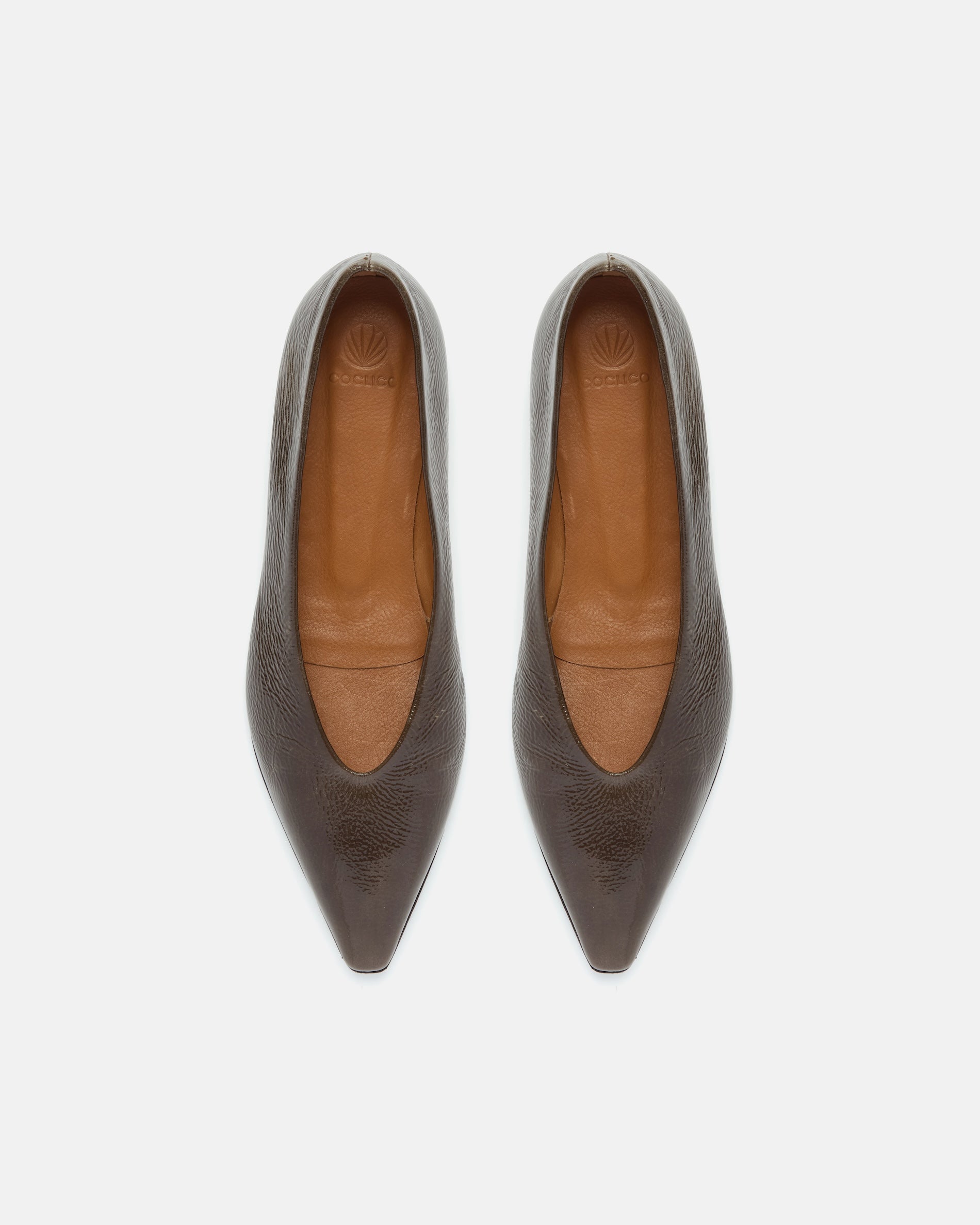 Pair of dark brown patent leather pointed-toe flat shoe on a light grey background