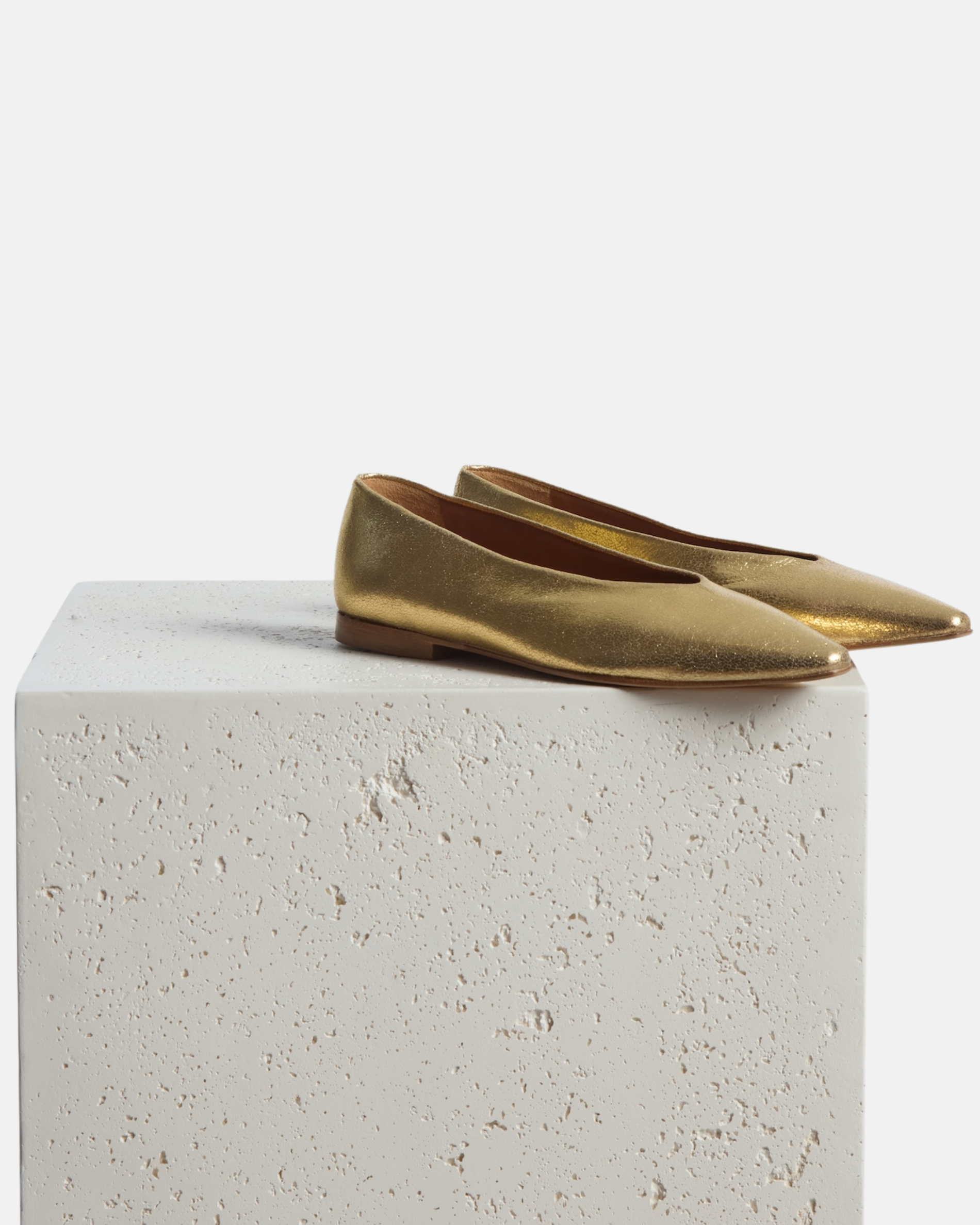Shoes on a pedestal: shimmering gold leather pointed-toe flat with clean lines and a flexible leather sole, on a white background.