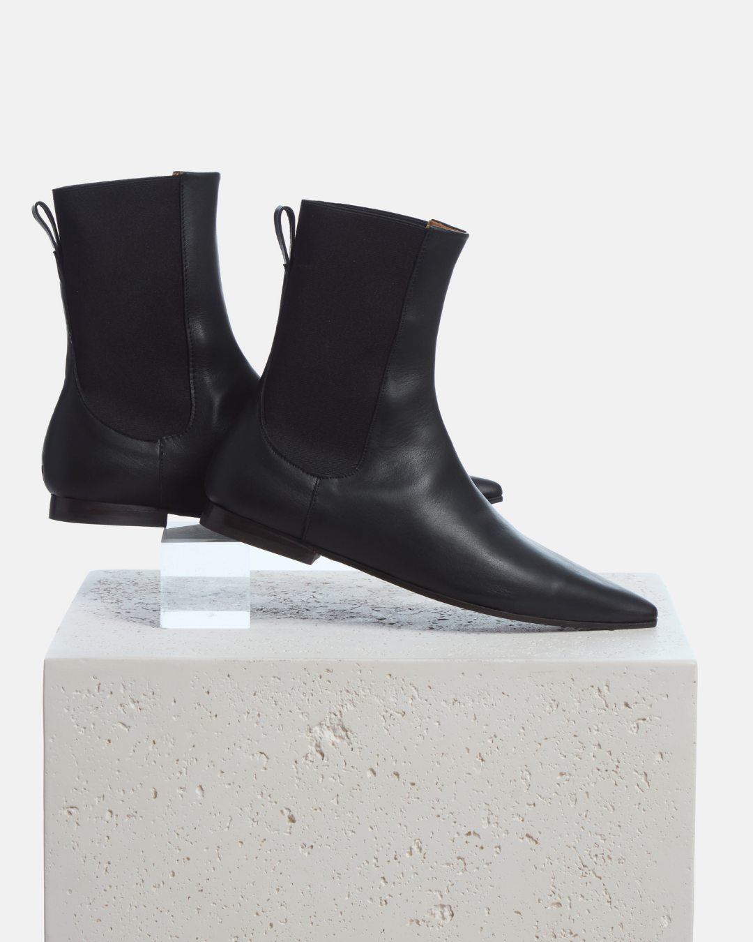 Coclico Cad Boot in black leather, flat pointed toe Chelsea boots styled on a stone plinth