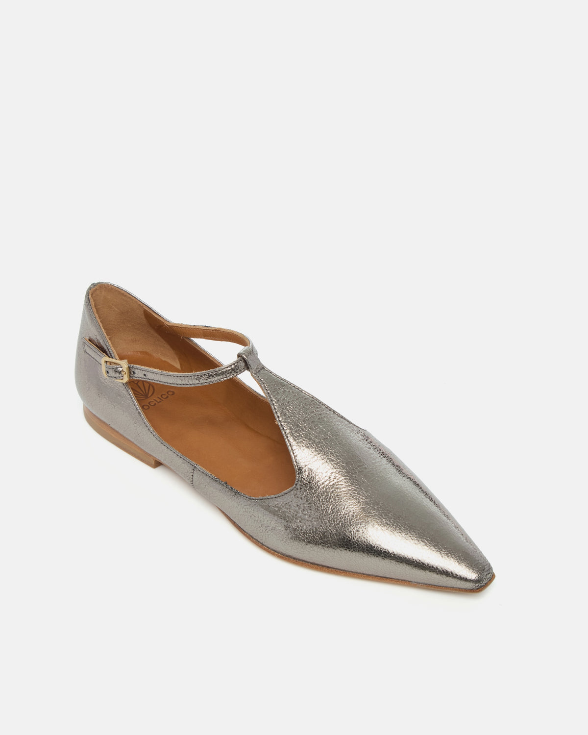 Angled view of a pointed-toe silvery metallic T-strap flat with adjustable buckle and leather sole on a white background
