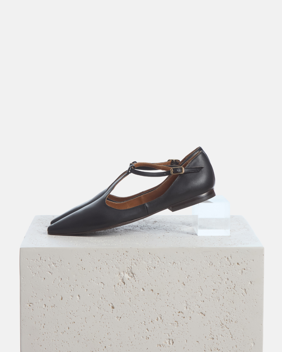 Coclico Celeste T-Strap Flat in black leather, T-strap flats styled on a stone plinth