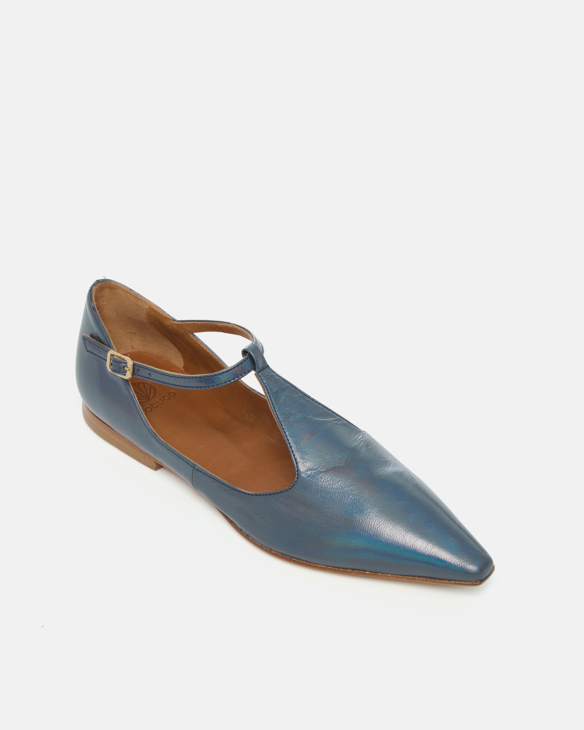 Angled view of a pointed-toe iridescent blue metallic T-strap flat with adjustable buckle and leather sole on a white background