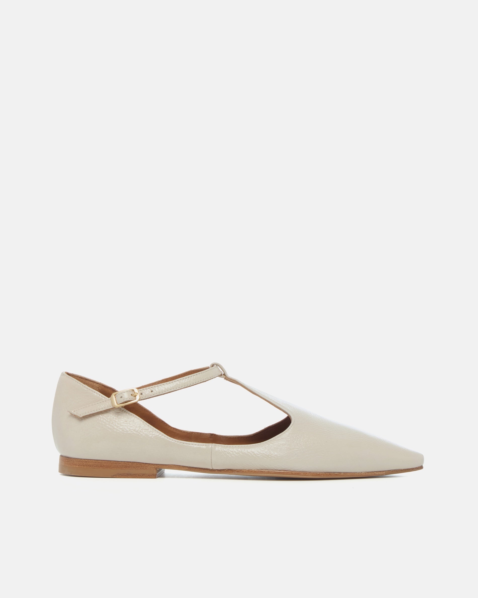 Side view of a pointed-toe off-white patent leather T-strap flat with adjustable buckle and leather sole on a white background
