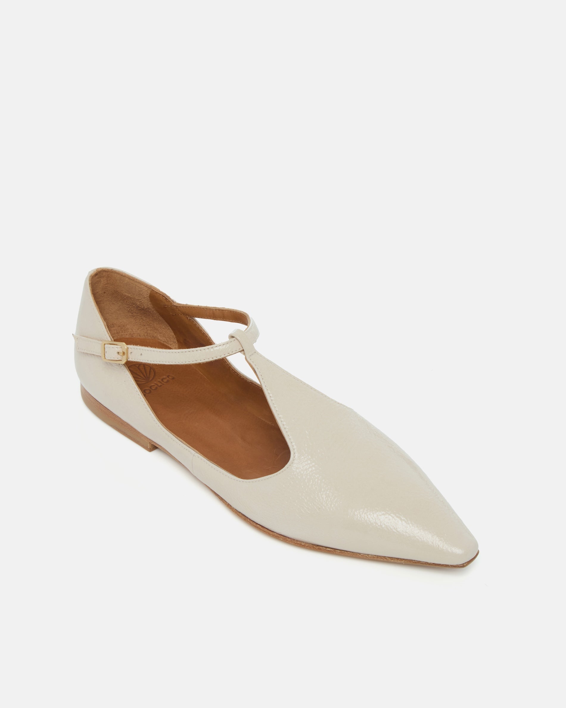 Angled view of a pointed-toe off-white patent leather T-strap flat with adjustable buckle and leather sole on a white background