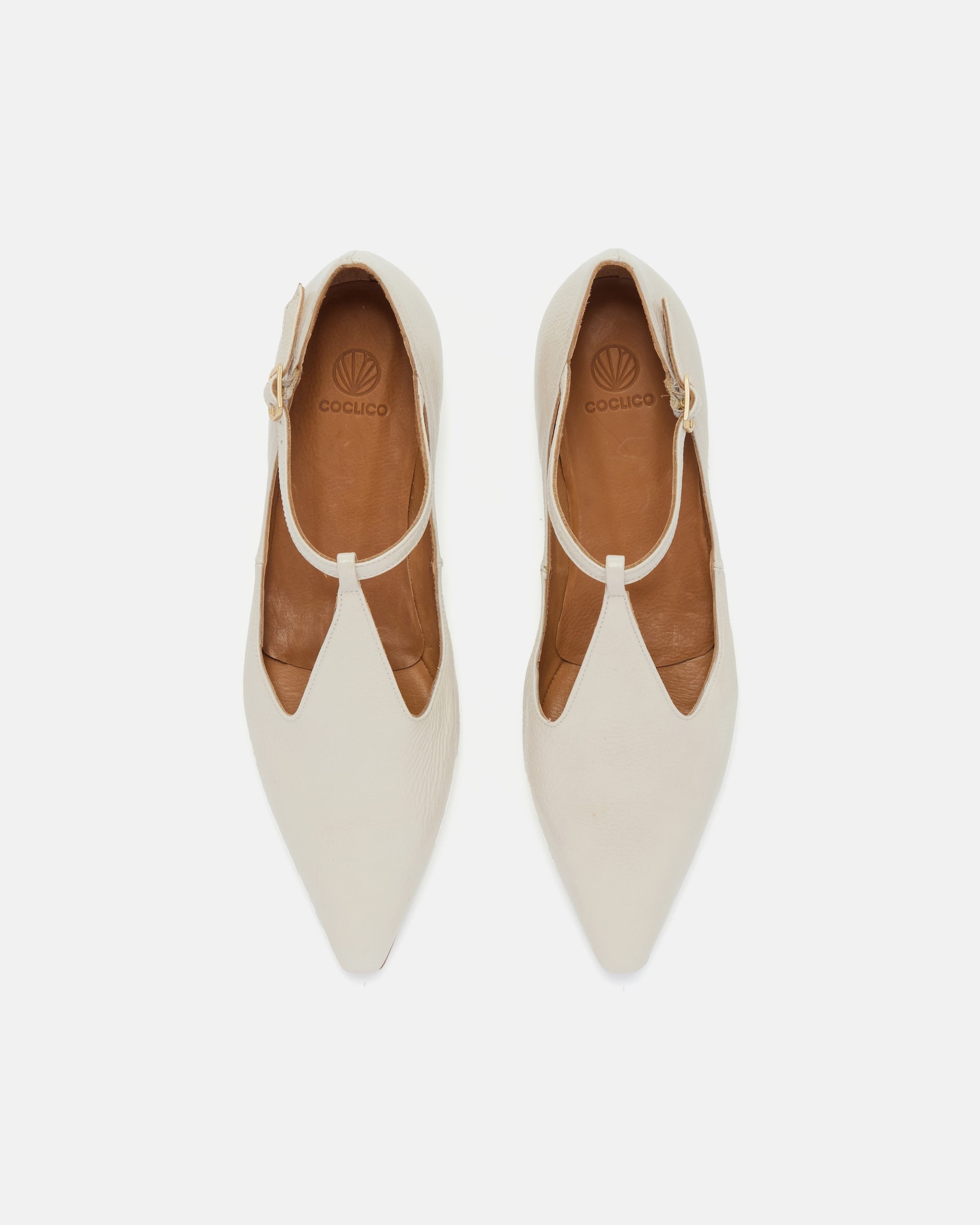 Top view of a pointed-toe off-white patent leather T-strap flat with adjustable buckle and leather sole on a white background