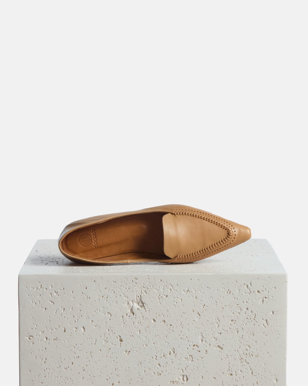 Shoe on a pedestal: pointed-toe camel leather loafer with topstitch detailing and a flat leather sole on a white background