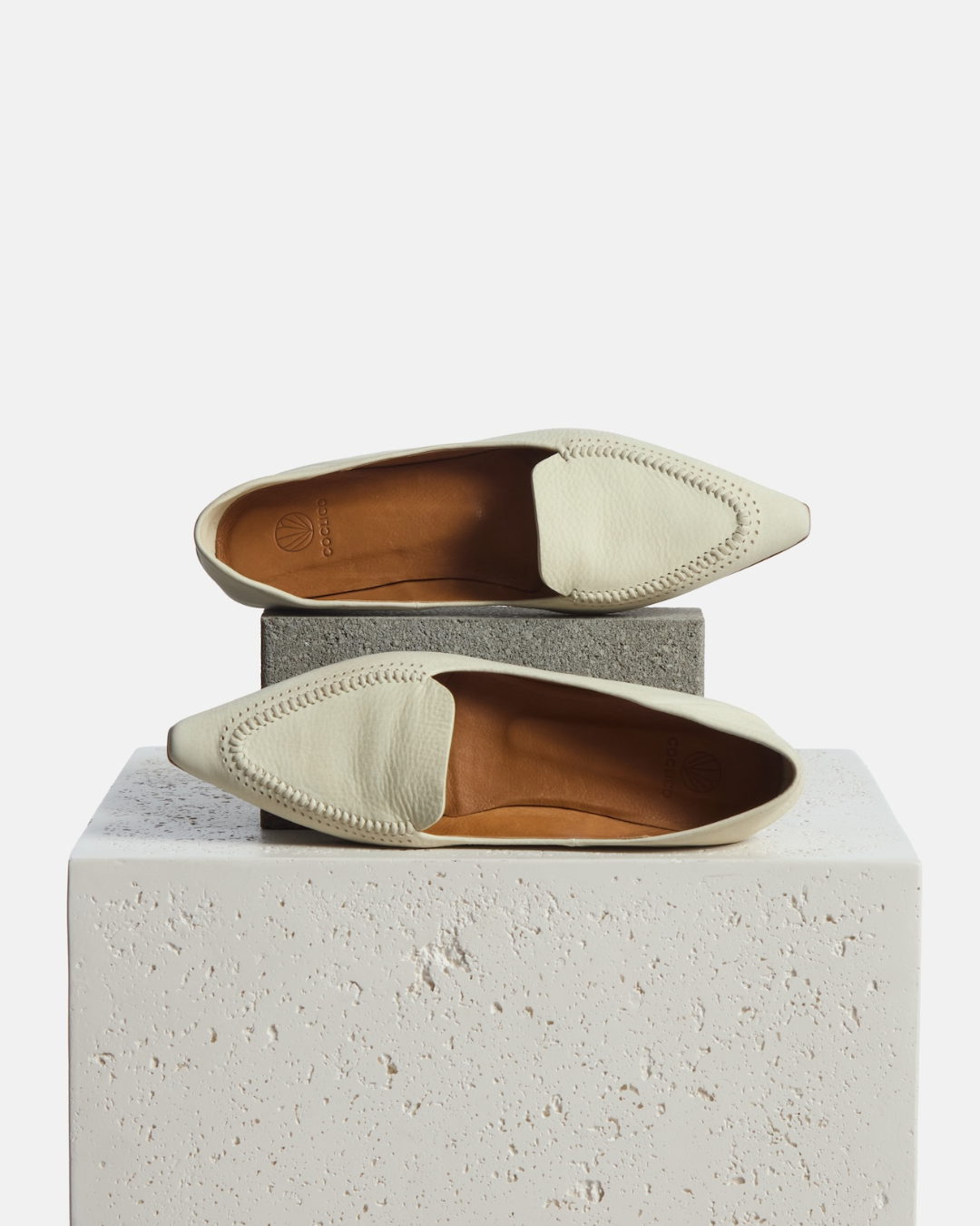 loafer on a plinth: pointed-toe white nubuck leather loafer with topstitch detailing and a flat leather sole on a white background