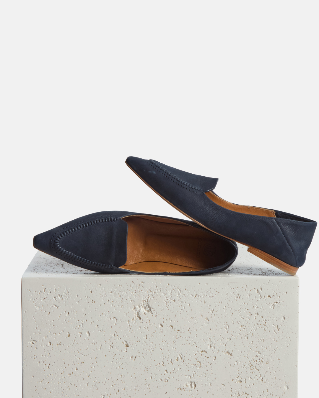 loafer on a plinth: pointed-toe navy nubuck leather loafer with topstitch detailing and a flat leather sole on a white background