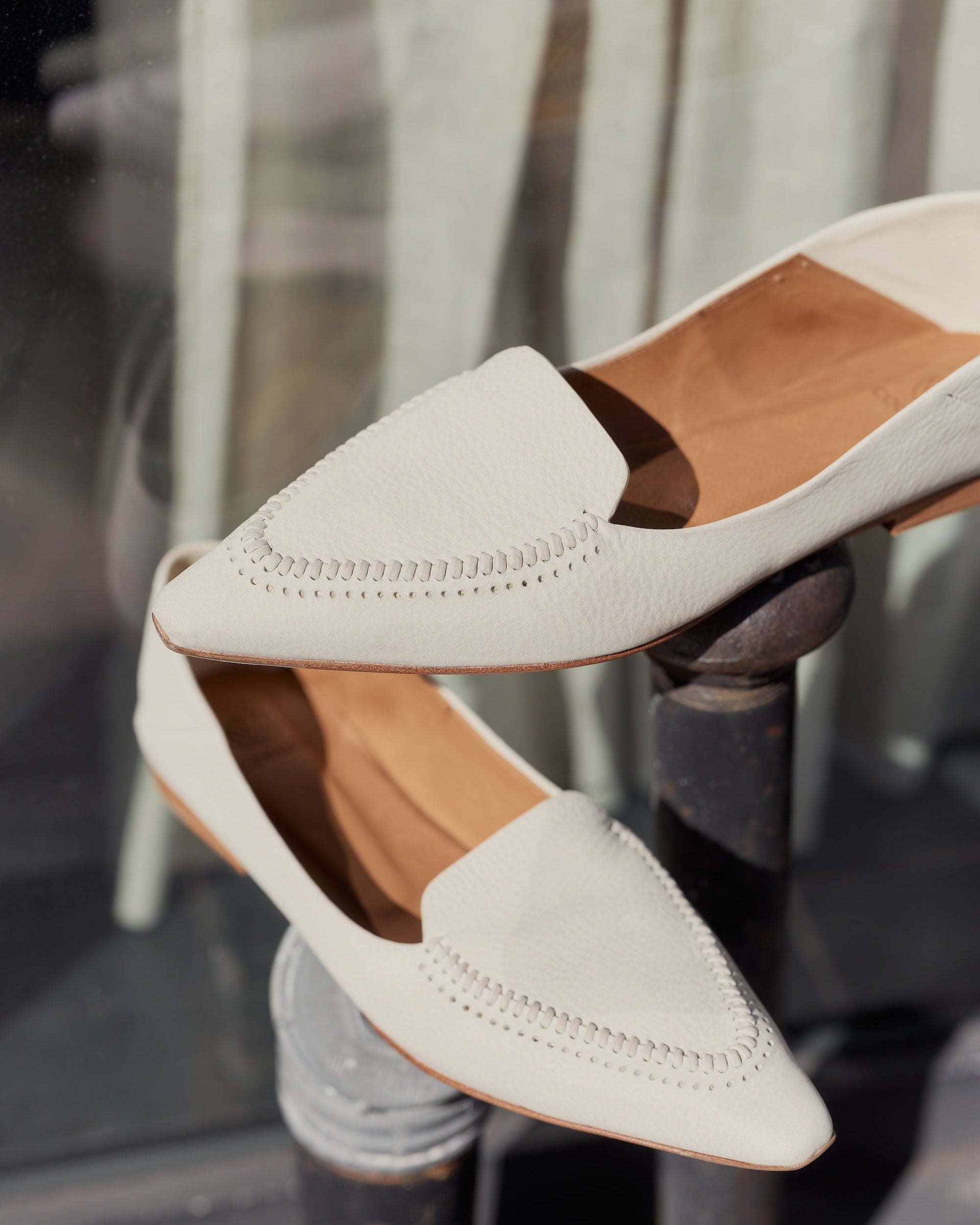 White pointed-toe shoes with brown soles on a blurred background