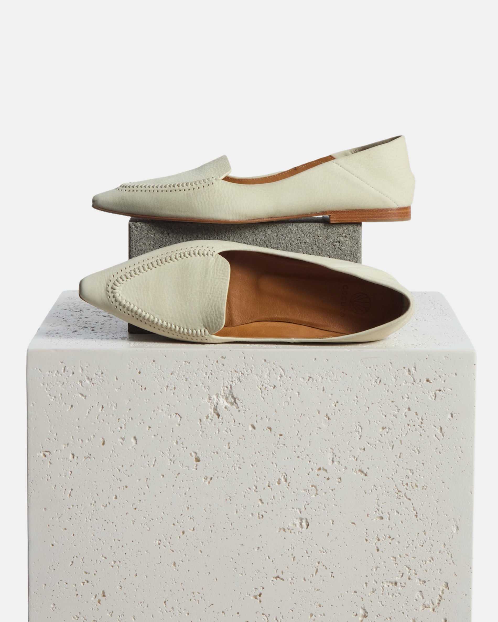 loafer on a plinth: pointed-toe white nubuck leather loafer with topstitch detailing and a flat leather sole on a white background