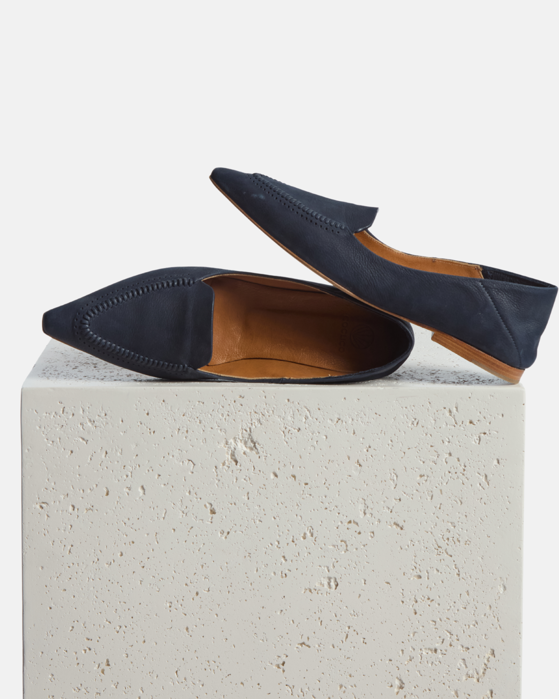 loafer on a plinth: pointed-toe navy nubuck leather loafer with topstitch detailing and a flat leather sole on a white background