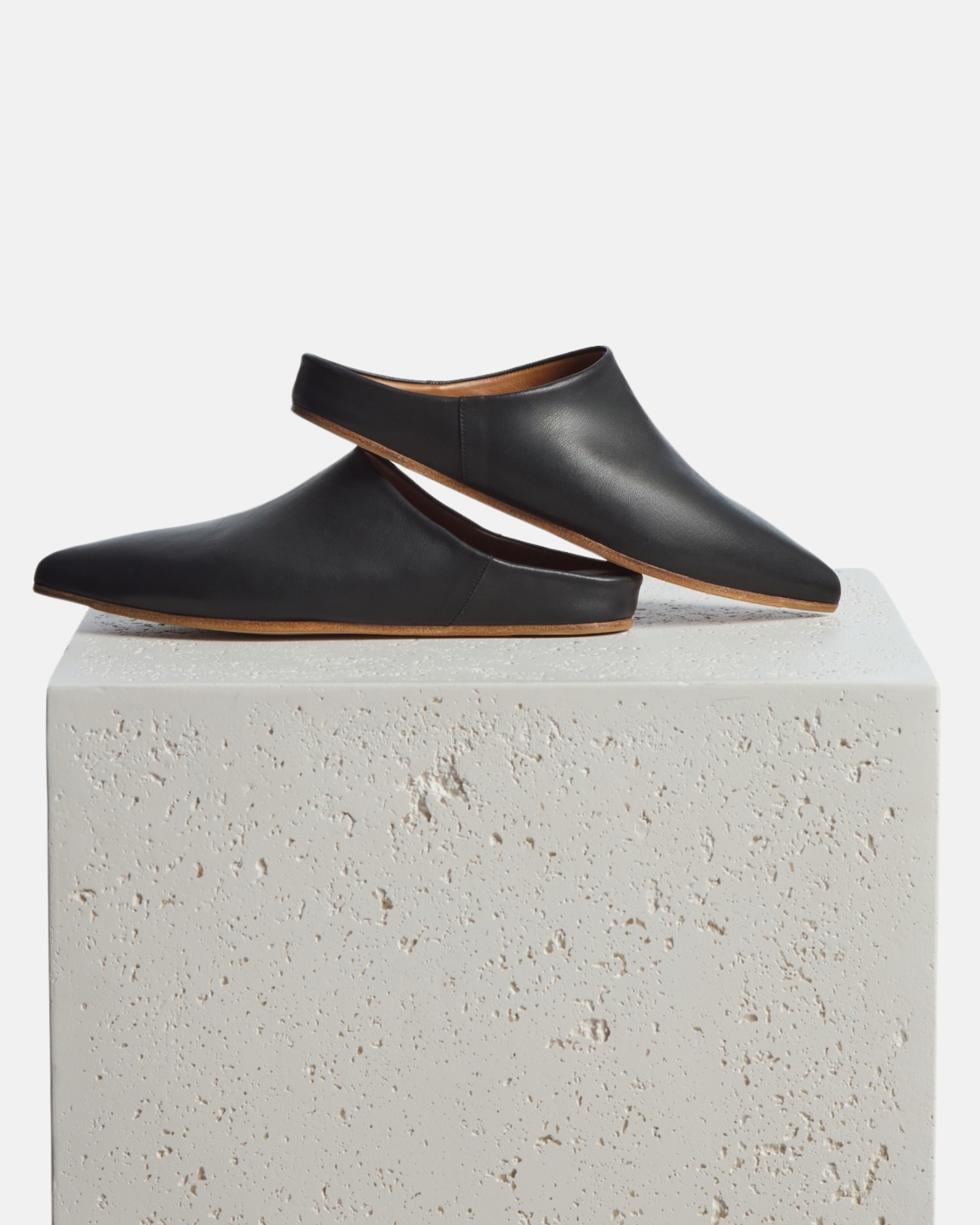 Shoes on a stone pedestal: black pointed-toe leather mule with a slight built-in wedge and clean minimalist silhouette on a white background