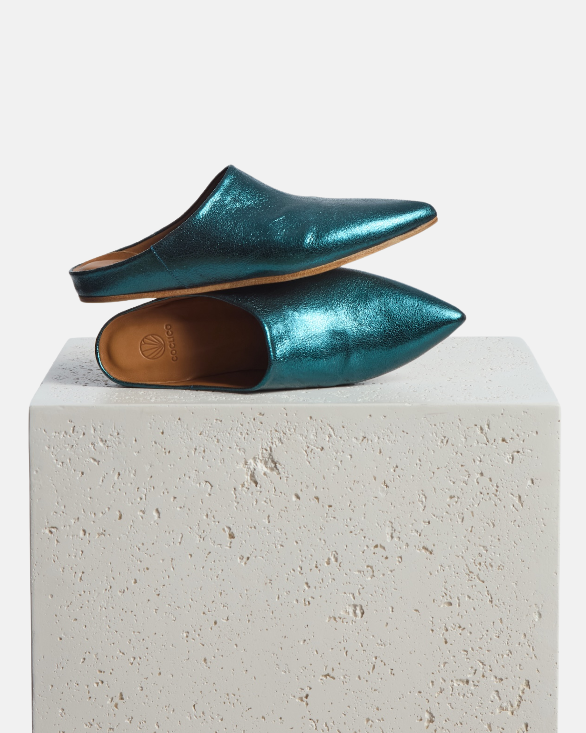 Shoes on a pedestal: blue metallic pointed-toe leather mule with a slight built-in wedge and clean minimalist silhouette on a white background