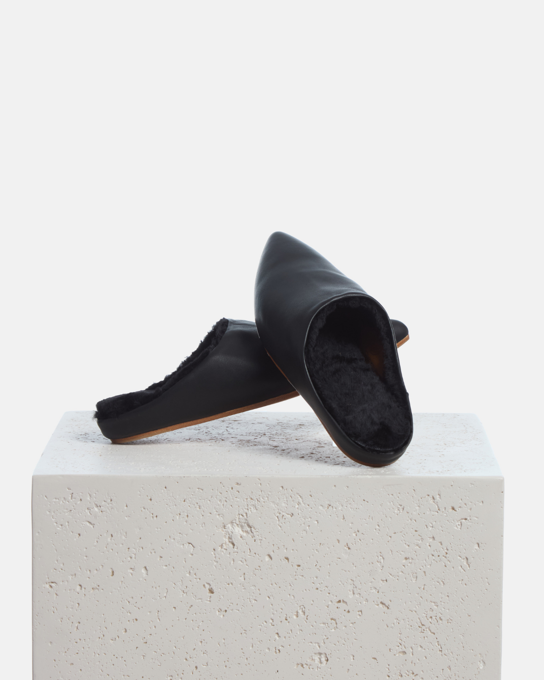 Coclico Dia Shearling Slide in black leather, shearling lined pointed toe mules styled on a stone plinth