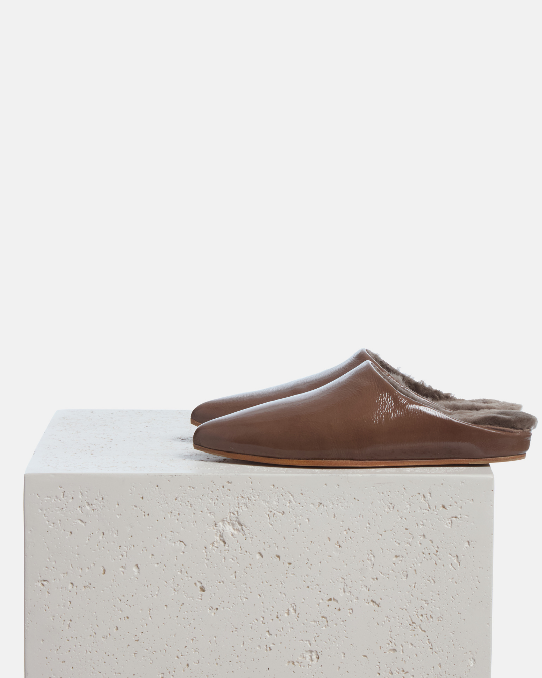 Coclico Dia Shearling Slide in Boue crinkled patent, shearling lined mules styled on a stone plinth