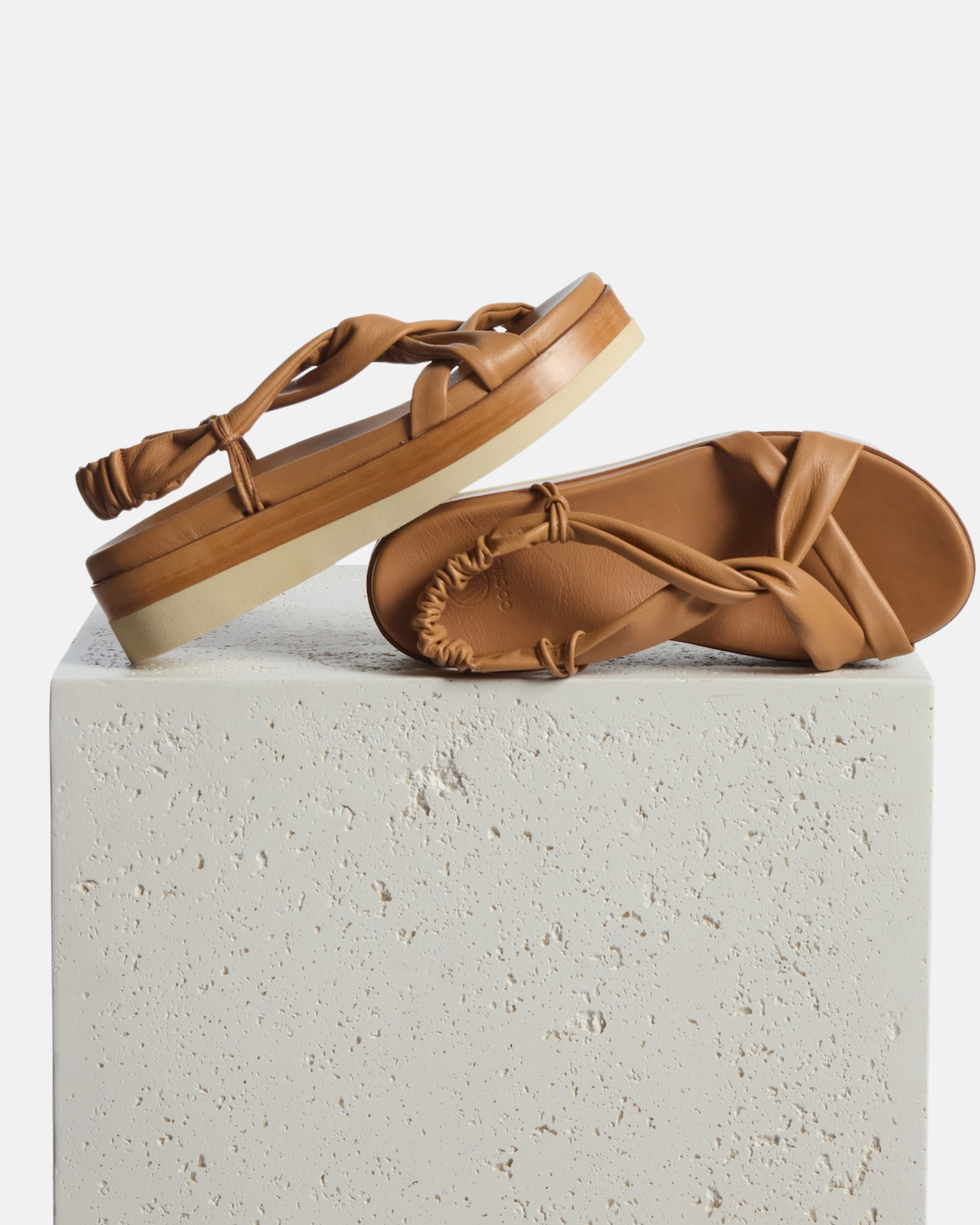 Shoe on plinth: pale brown leather wedge sandal with softly twisted straps, elasticized back strap, and a lightweight EVA platform sole