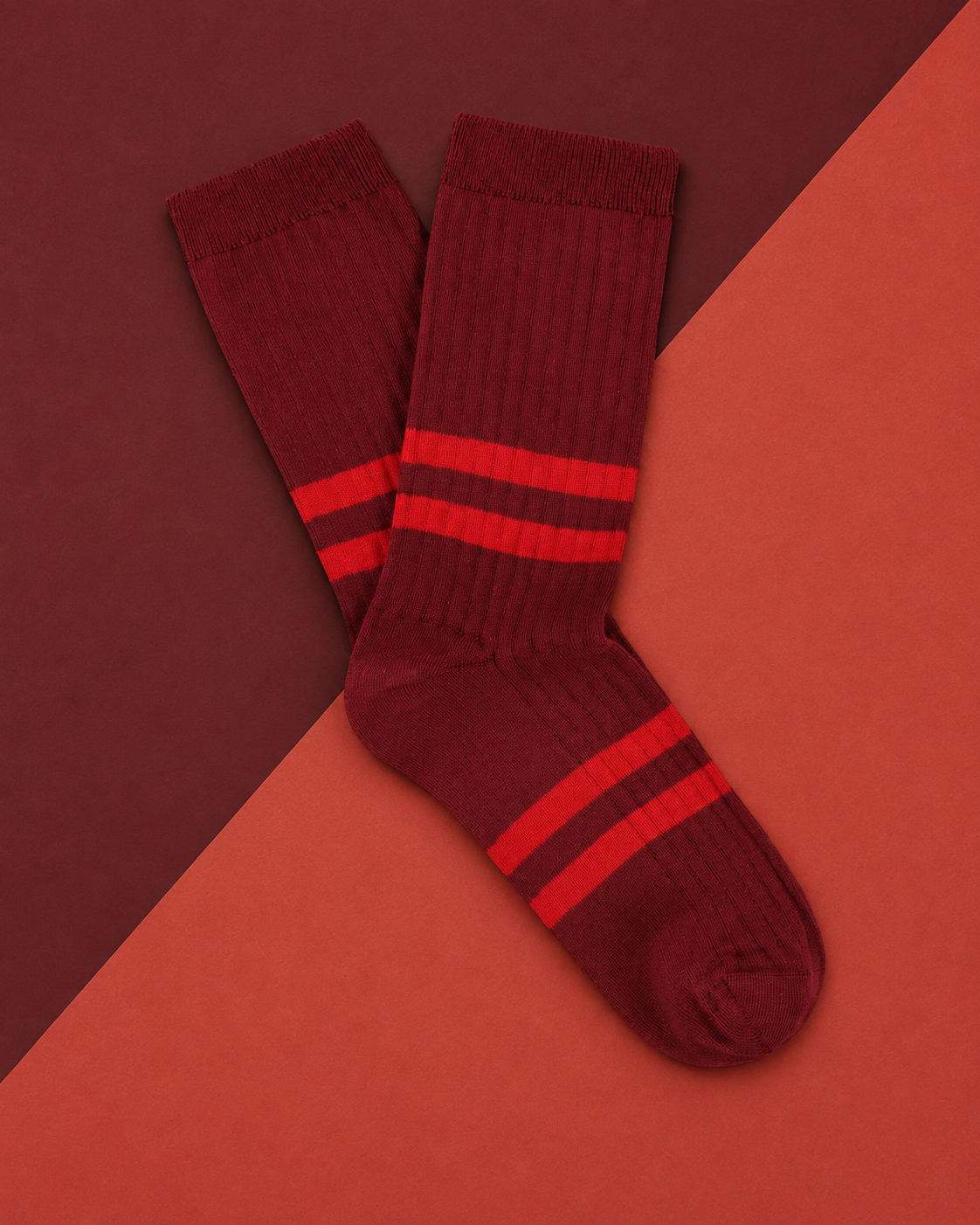 Escuyer striped socks in Bordeaux with red stripes, laid flat on a two-tone red background