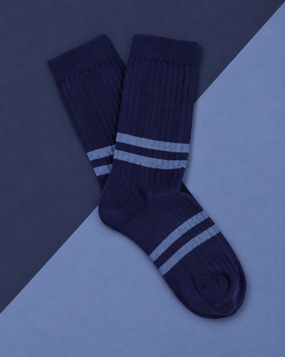 Escuyer striped socks in navy with light blue stripes, laid flat on a two-tone blue background