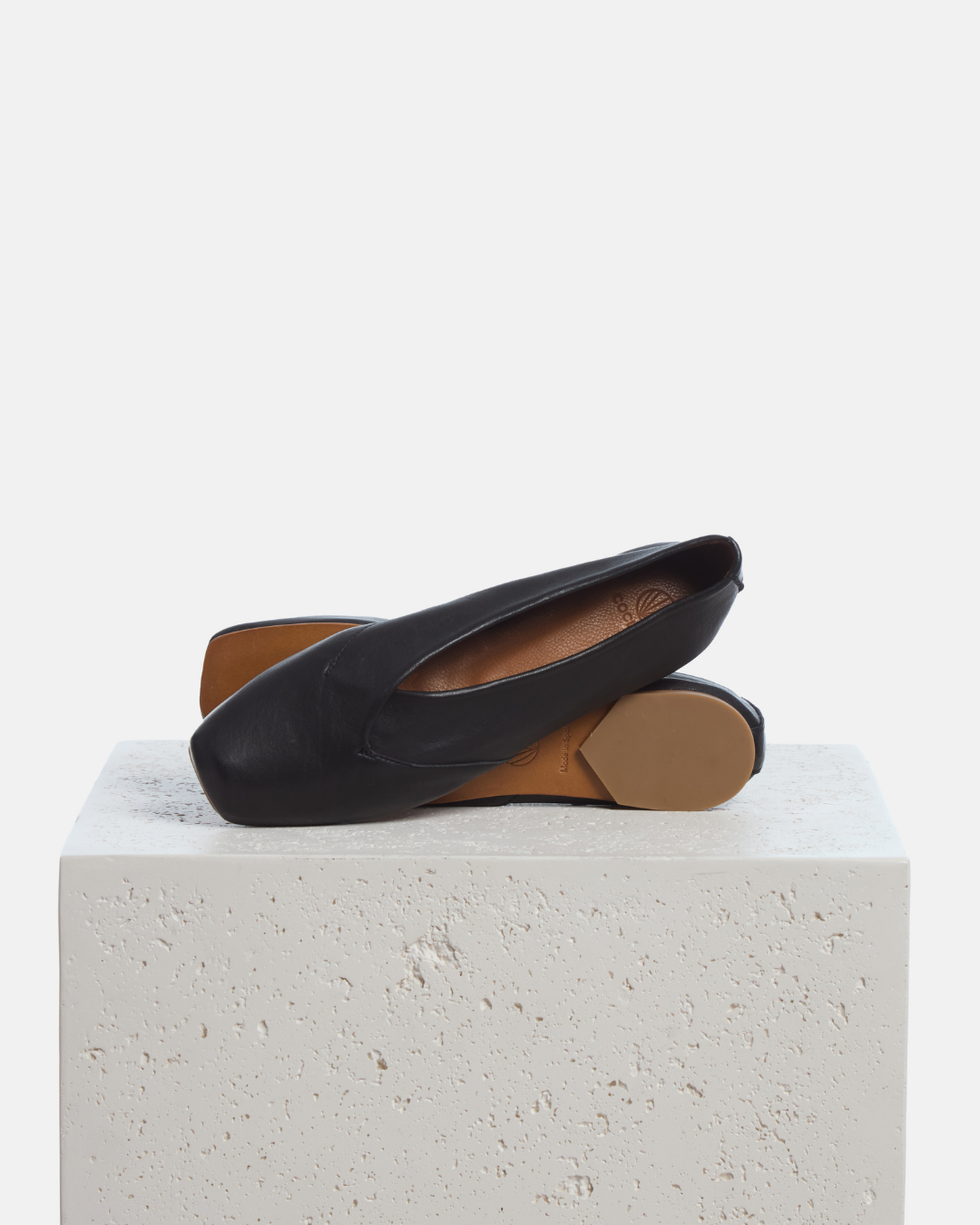 Coclico Franklin Flat in black leather, soft ballet flats styled on a stone plinth