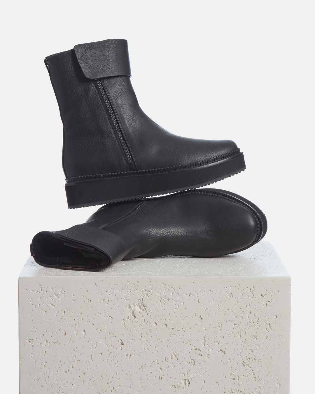 Coclico Greer Shearling Boot in black leather, shearling lined platform ankle boots styled on a stone plinth