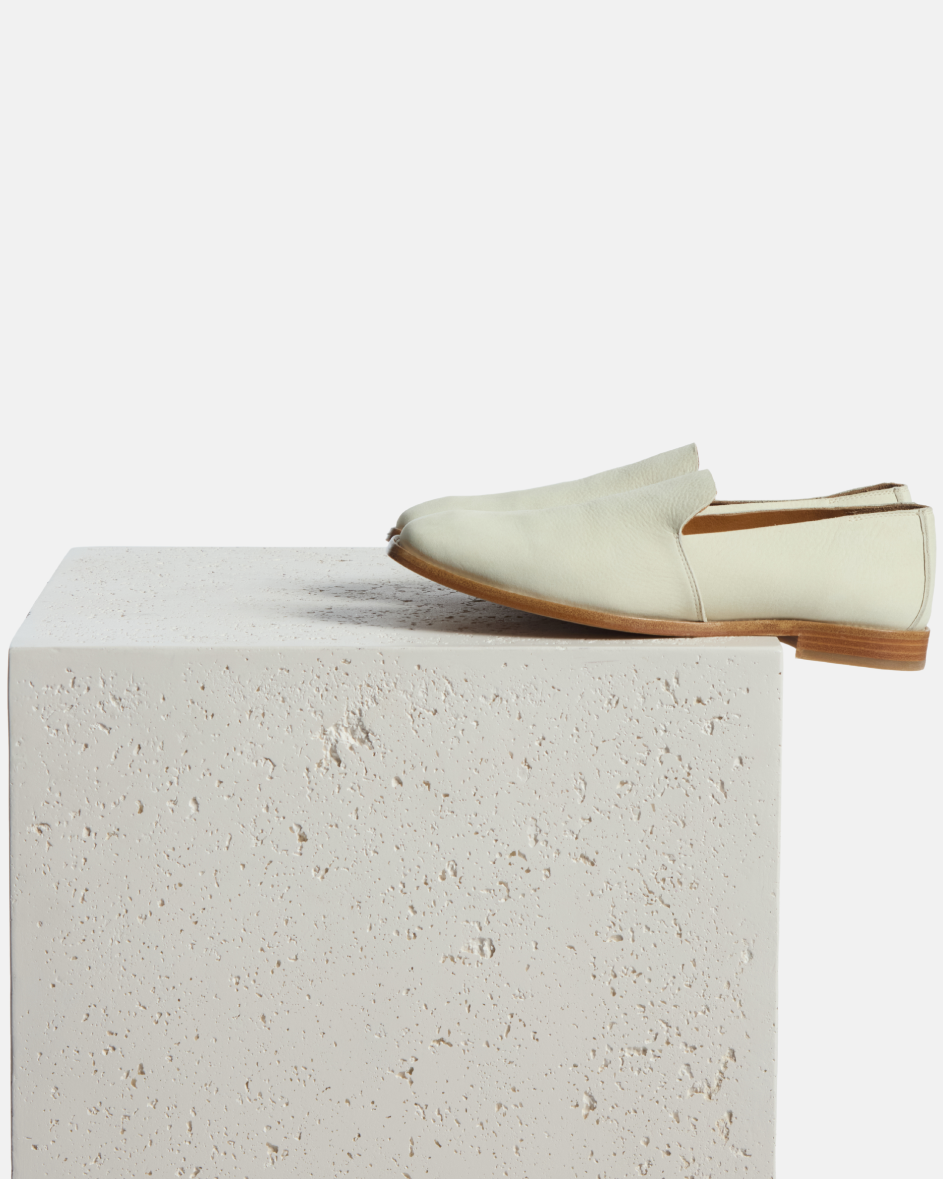 loafer on a plinth:  white nubuck leather slip-on loafer with a tapered square toe and low stacked heel on a white background