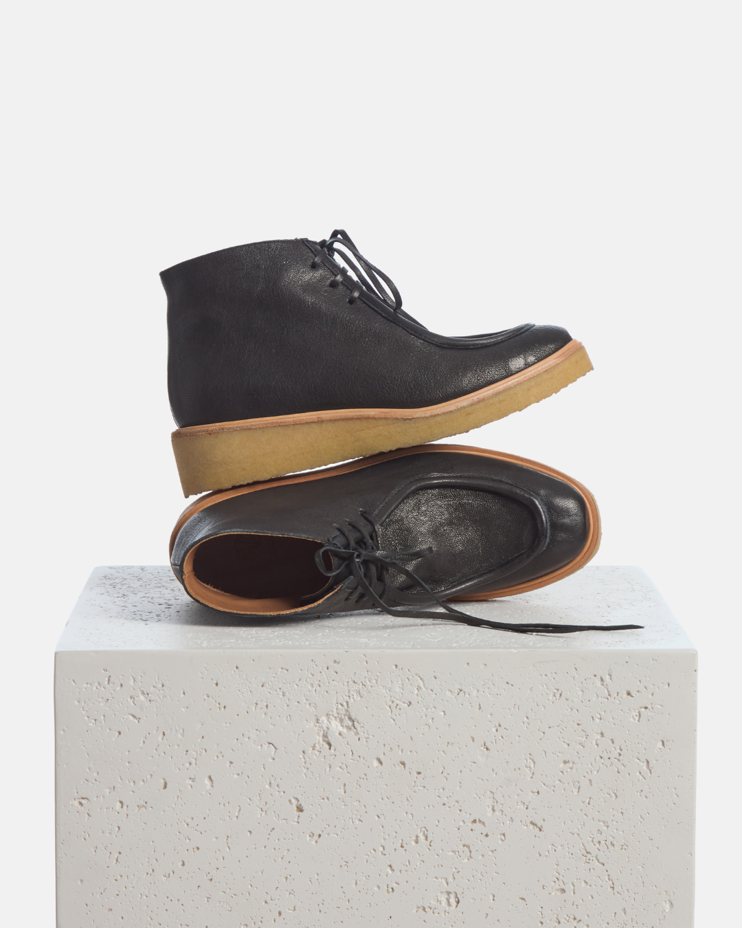 Coclico Hester Boot in black leather, lace up moc toe ankle boots with natural crepe soles styled on a stone plinth