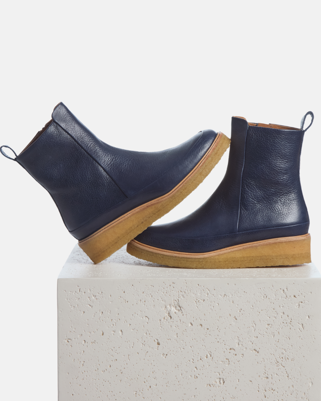 Coclico Hip Boot in Marino, navy leather crepe sole ankle boots styled on a stone plinth
