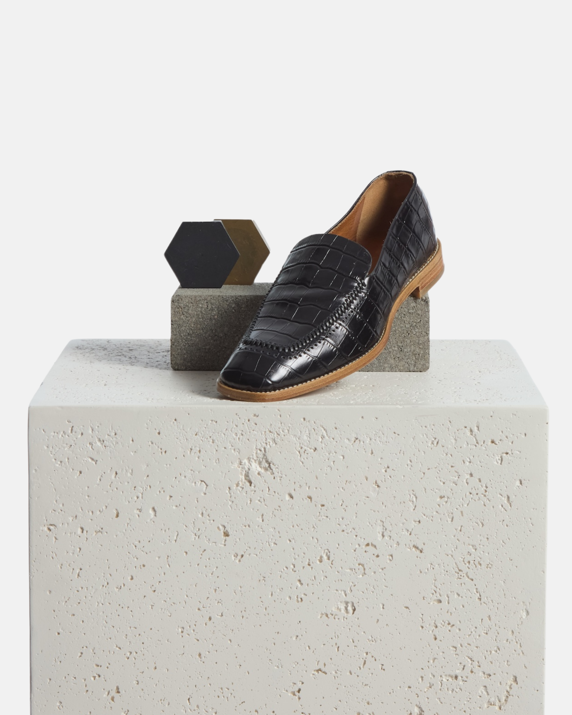 Loafer on a plinth:  black croc-embossed leather loafer with a softly squared toe and low stacked heel on a white background