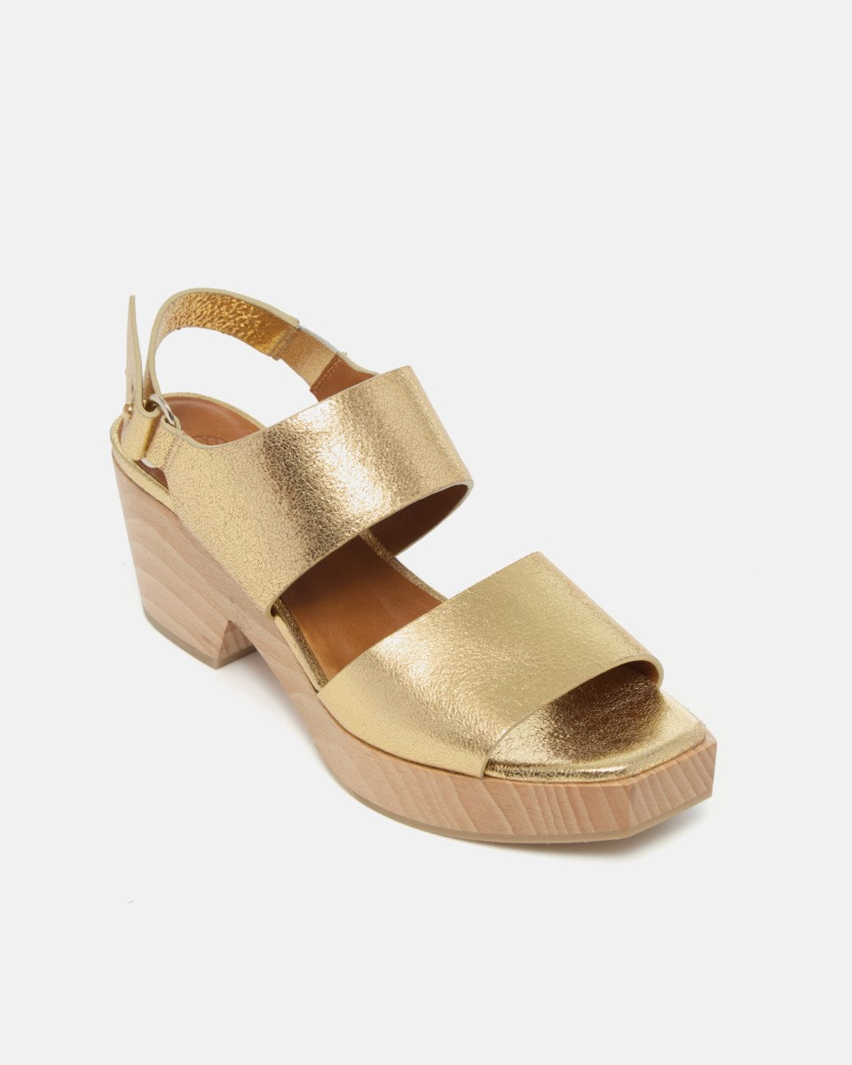 Angled view of a gold leather clog sandal with wide straps, adjustable slingback, squared toe, and solid ash wood block heel on a white background.