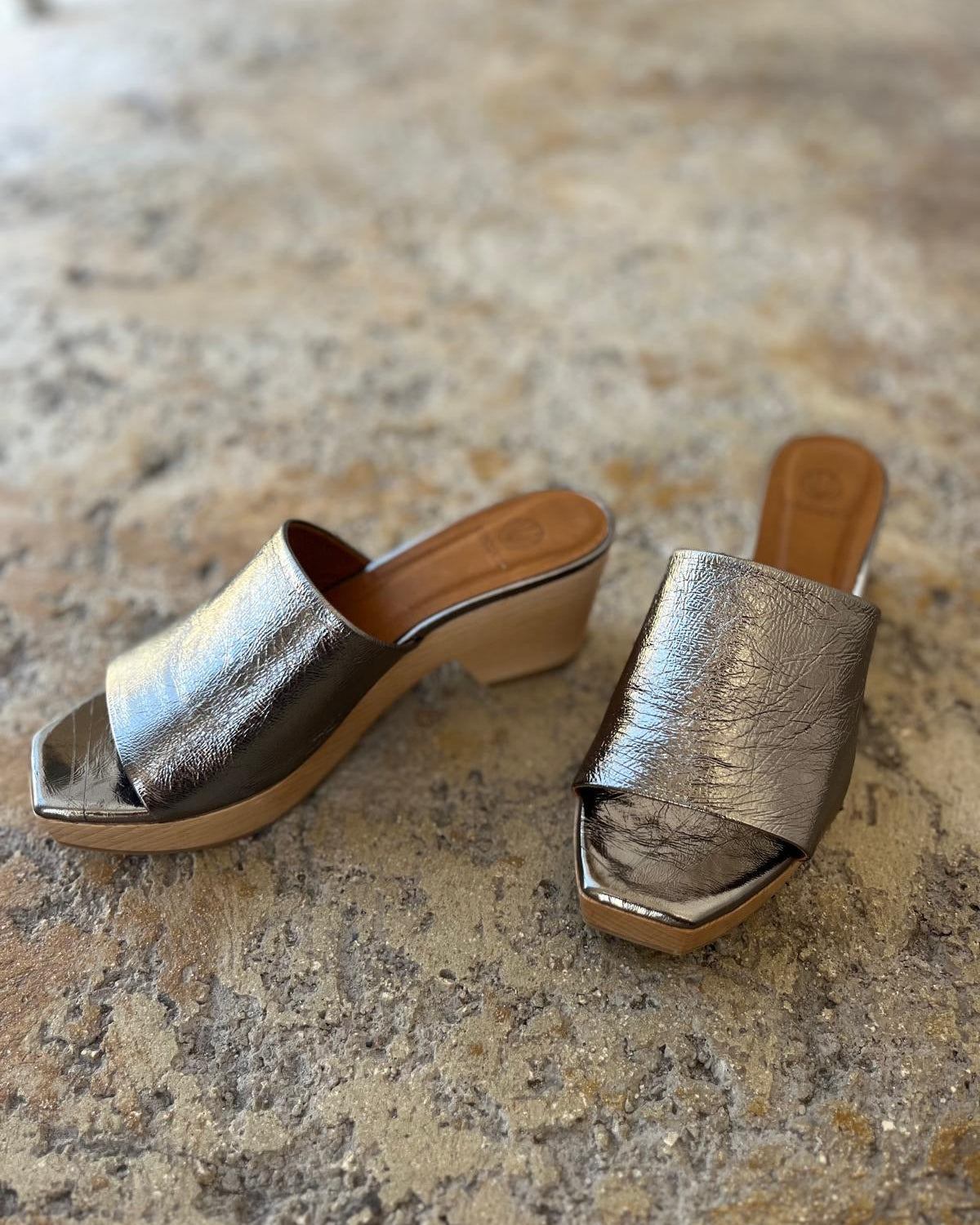 Pair of metallic slide clog sandals on a stone surface