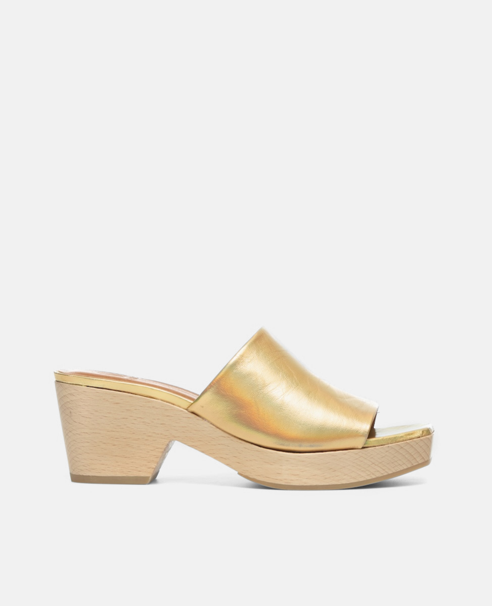 A gold, open-toe mule sandal with a smooth, metallic finish features a wide strap and a light wooden block heel.
