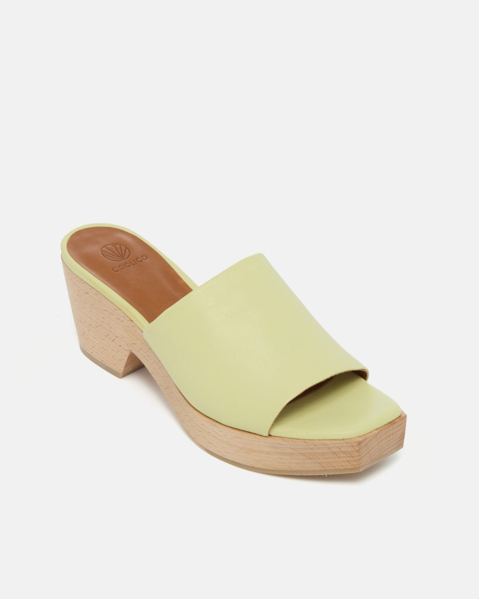 Angled view of a lemon yellow leather slide clog sandal with a wide upper, squared toe, and solid ash wood sole on a white background.