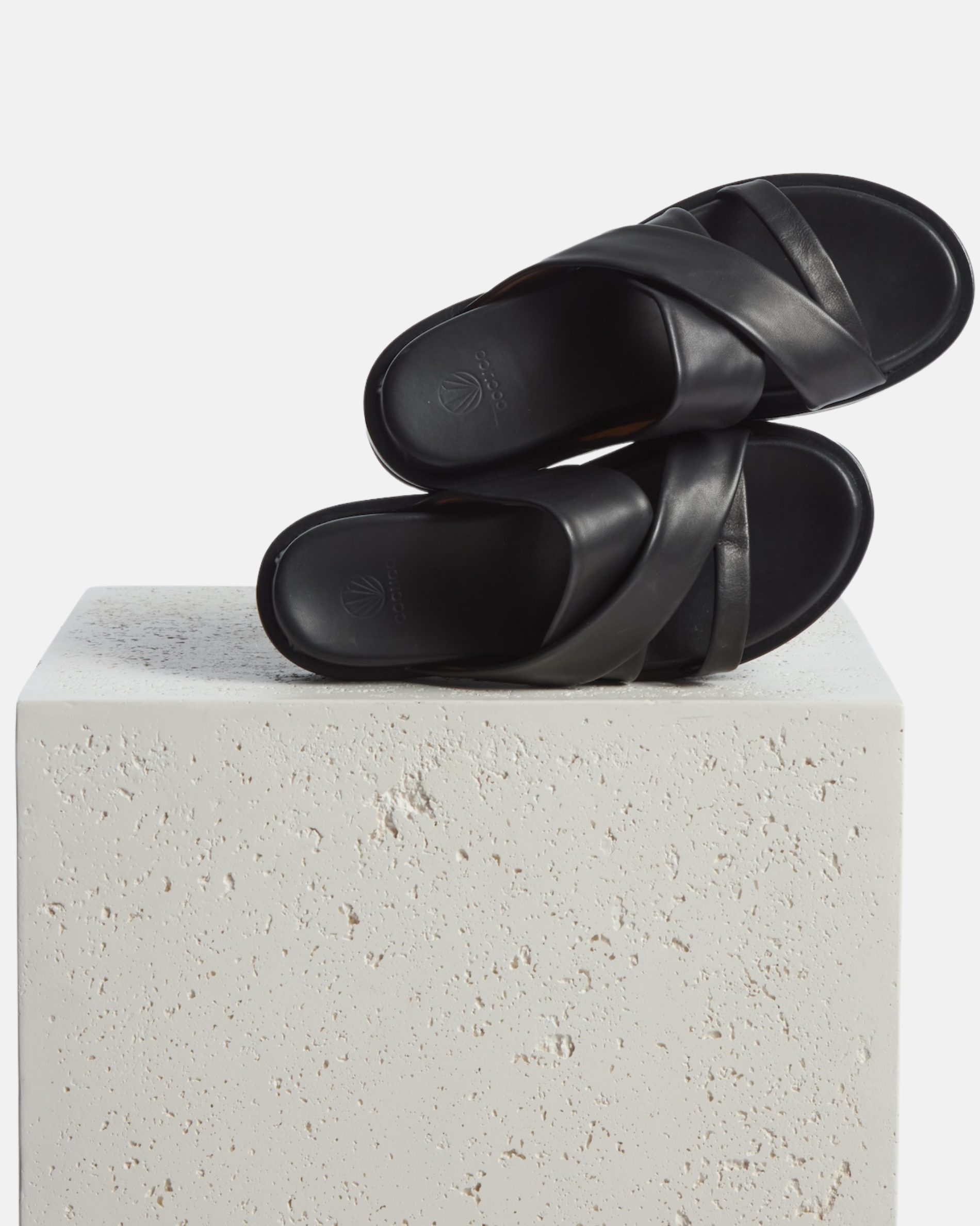 shoe on plinth: black leather footbed sandal with wide folded straps and a sleek cushioned platform sole