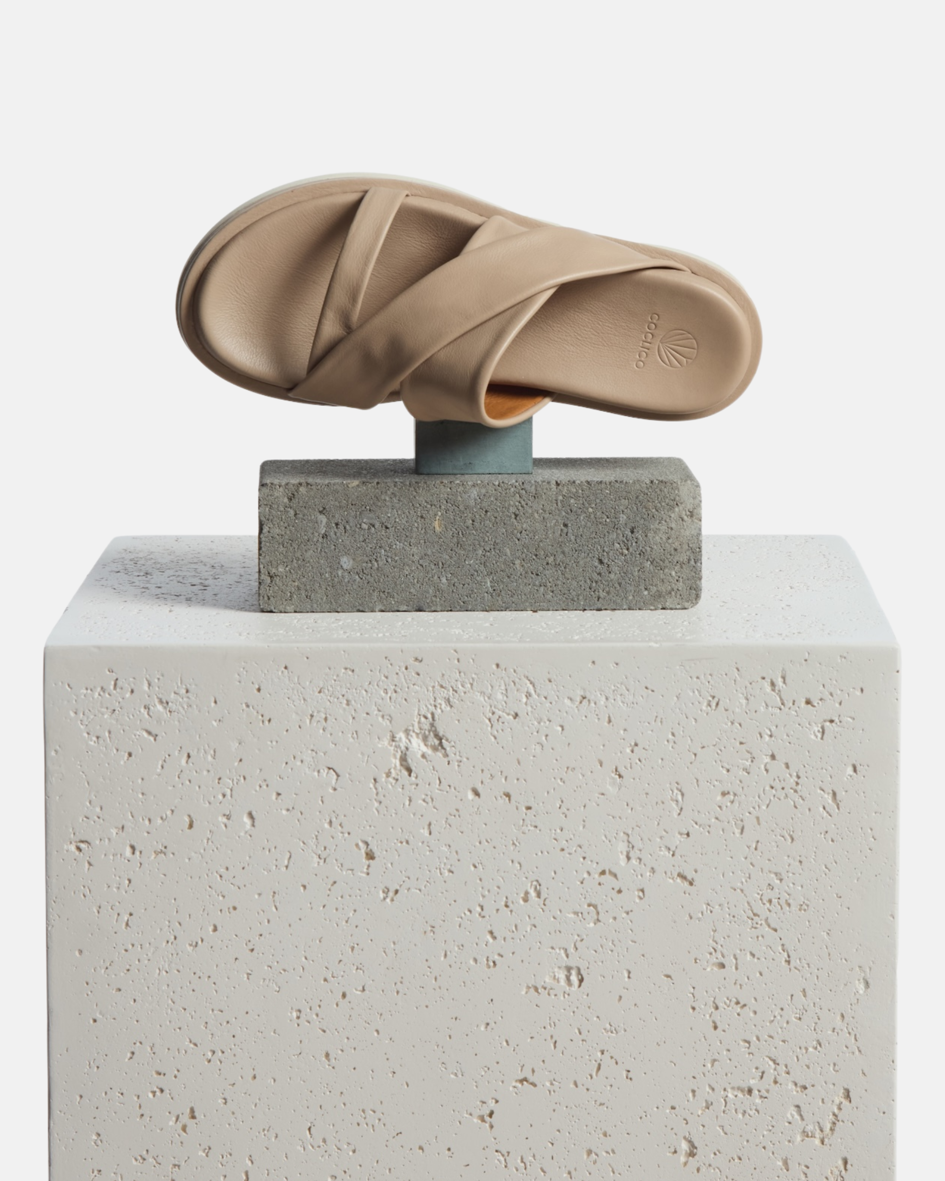 A slide sandal arranged on a plinth: grey leather footbed sandal with wide folded straps and a sleek cushioned platform sole