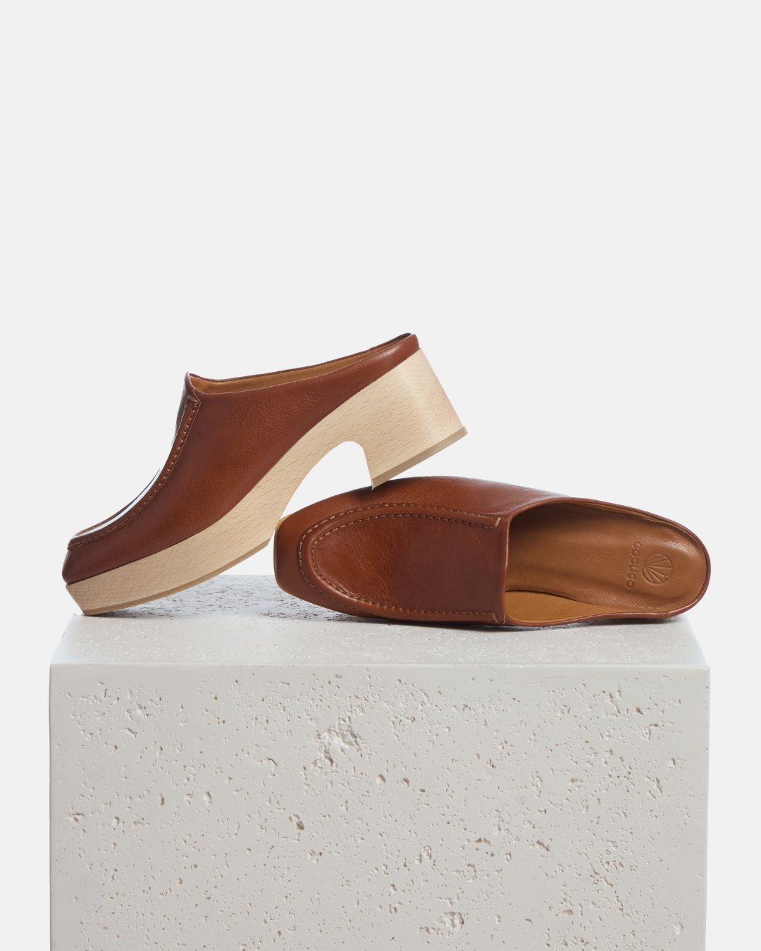Coclico Qadira Clog in Cuero, tan leather clog mules on natural wood bases styled on a stone plinth
