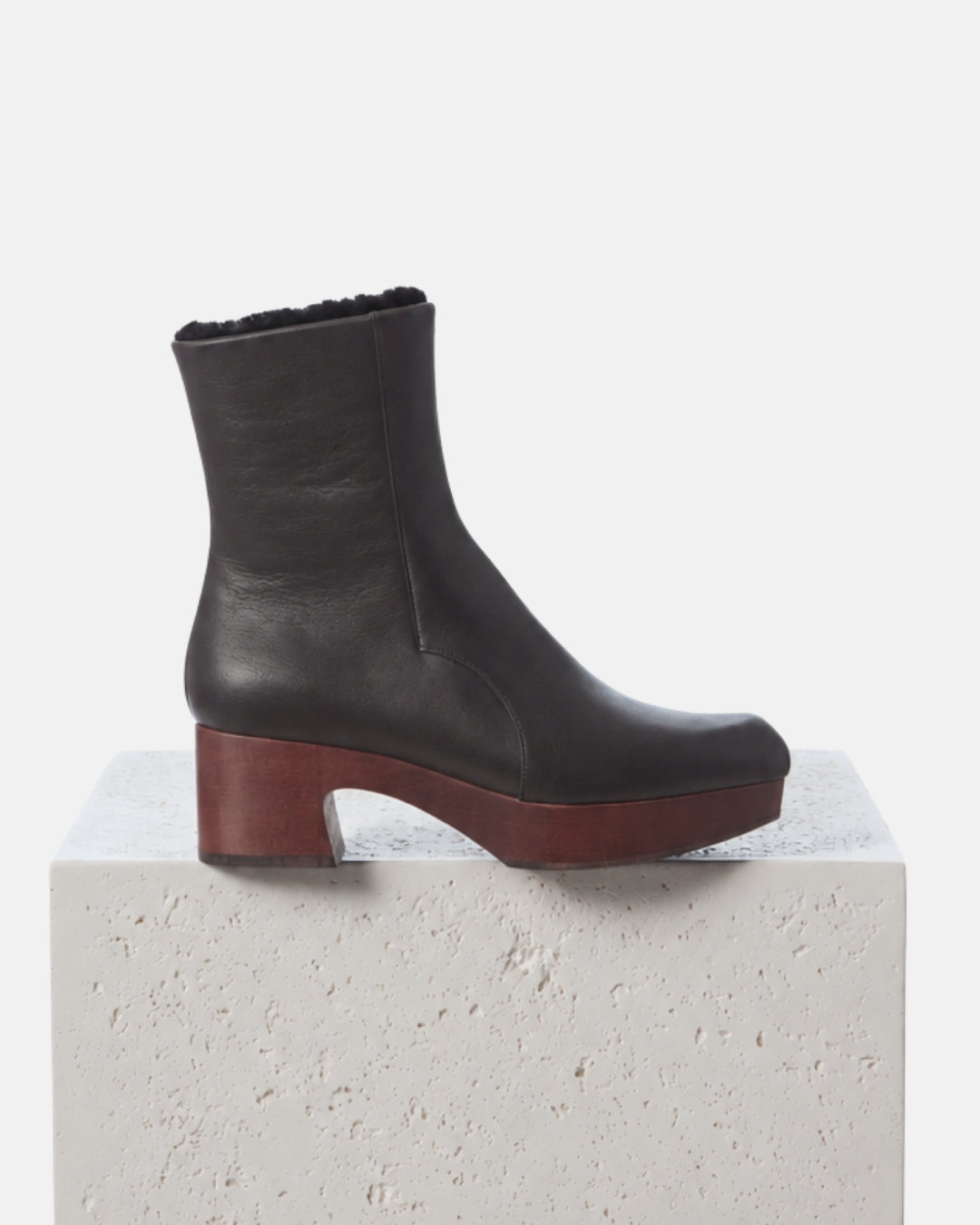 The Queen Shearling Clog Boot in Black leather and black shearling displayed on a white plinth
