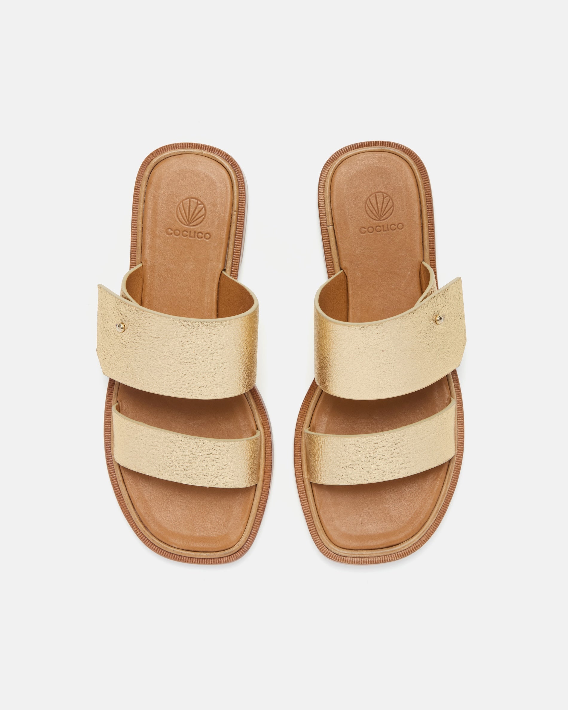 Top view of a gold metallic leather slide sandal with two wide straps, a subtle metal peg detail, cushioned leather footbed, and flat leather sole