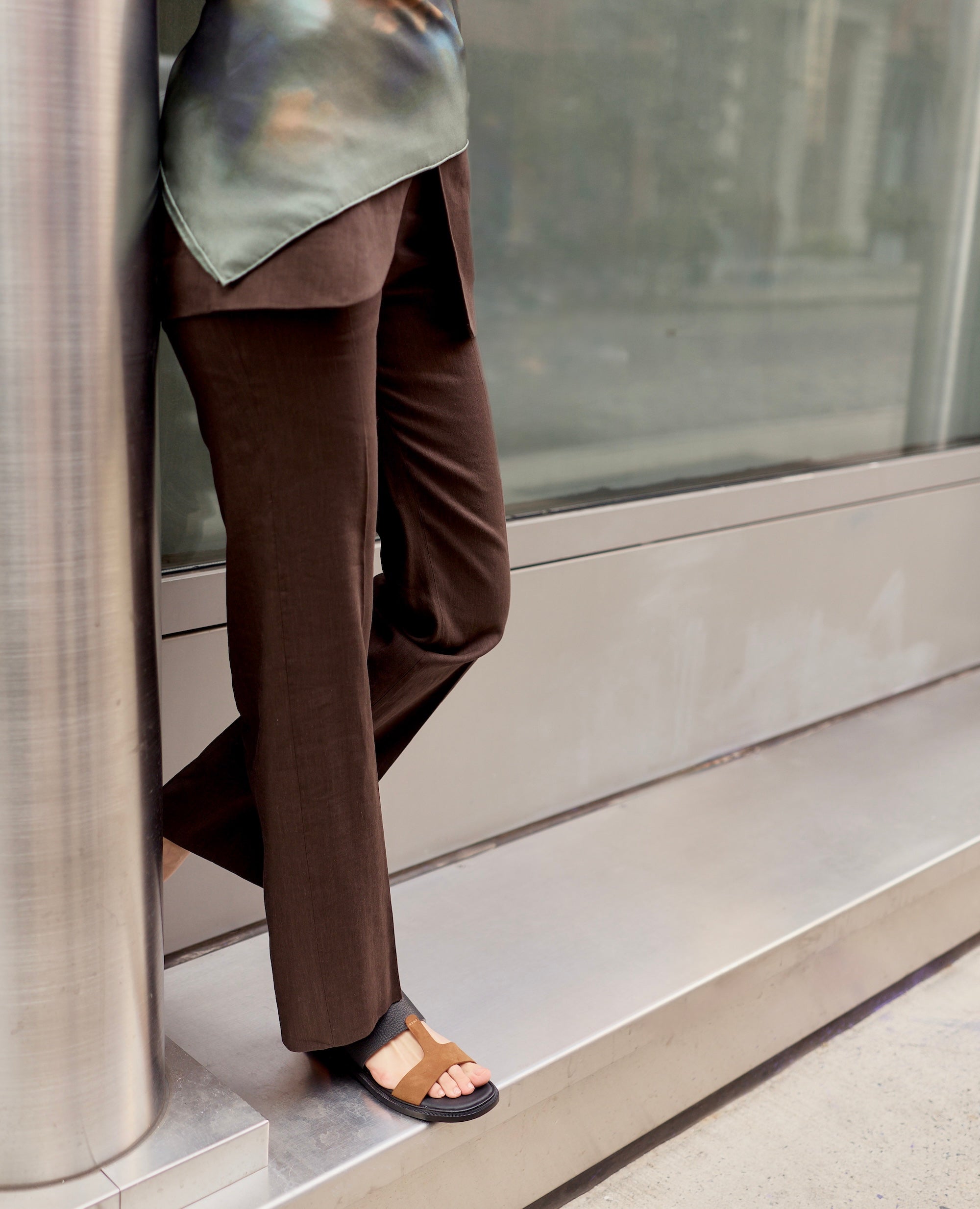 Person wearing brown pants and black and brown flat sandals standing on a step.