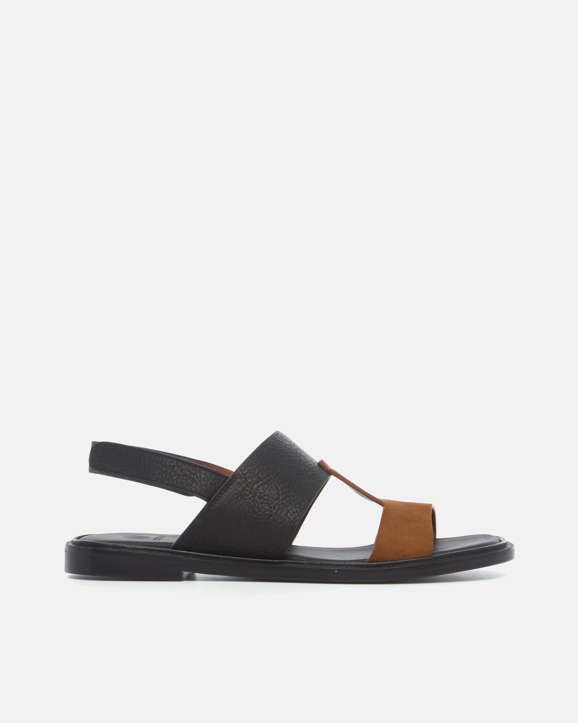 Side view of a two-tone leather slide sandal with wide black and brown straps, slim slingback strap, cushioned leather footbed, and flat sole.