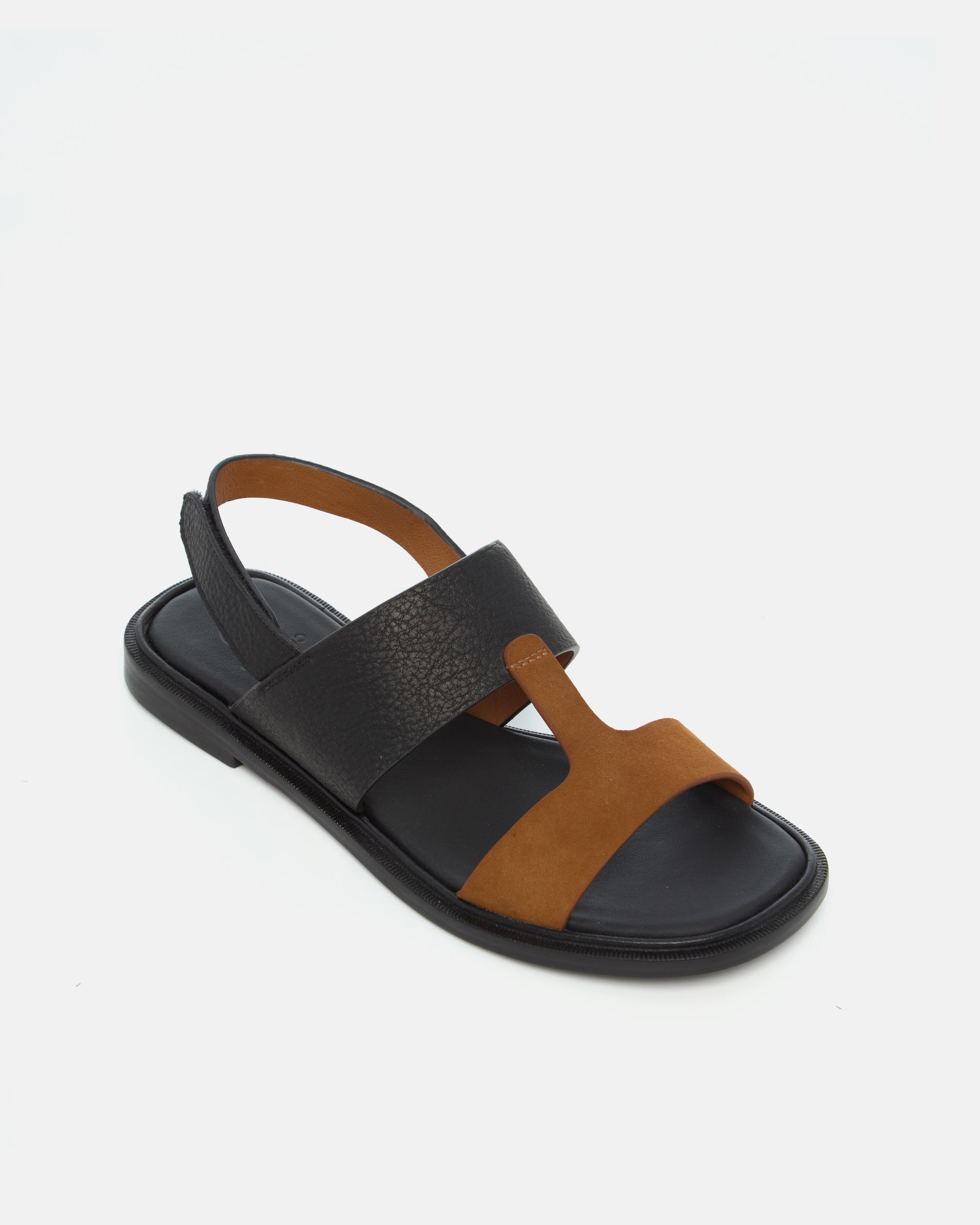 Angled view of a two-tone leather slide sandal with wide black and brown straps, slim slingback strap, cushioned leather footbed, and flat sole.