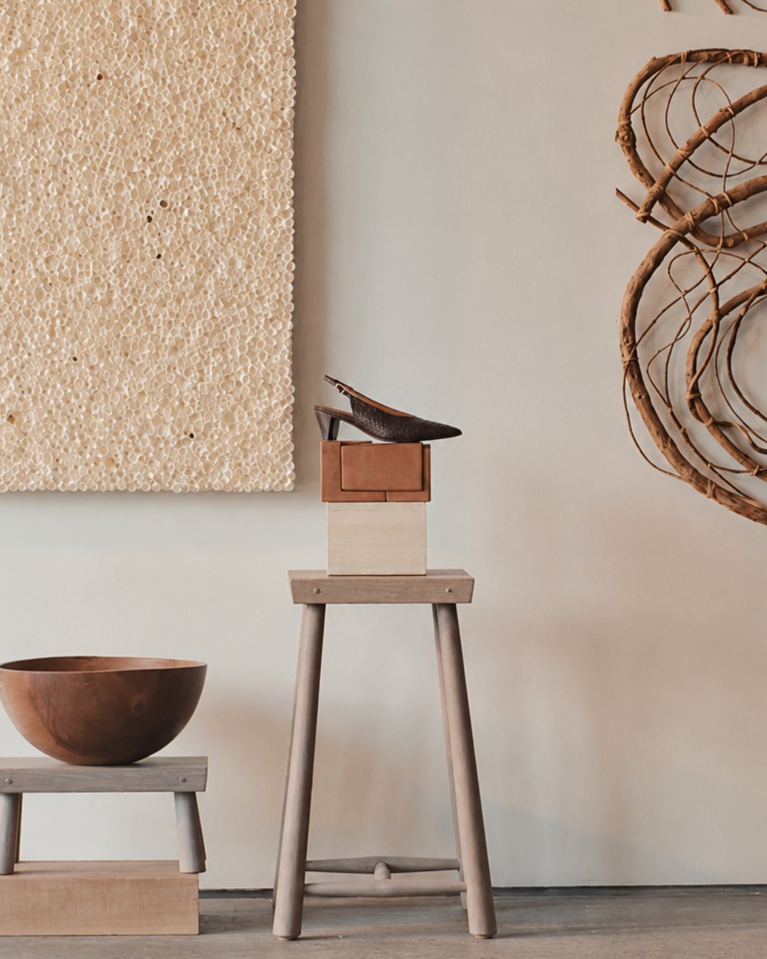 A dark brown snake leather slingback pump shoe displayed on top of a small wooden block and stool in a styled interior setting with neutral walls and decorative wood elements.