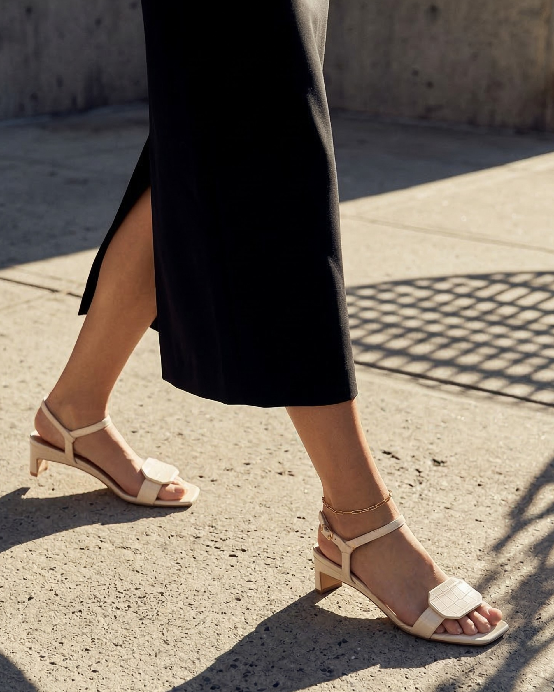 A person wears a Coclico croc embossed heeled sandal and black skirt as they walk in the city.